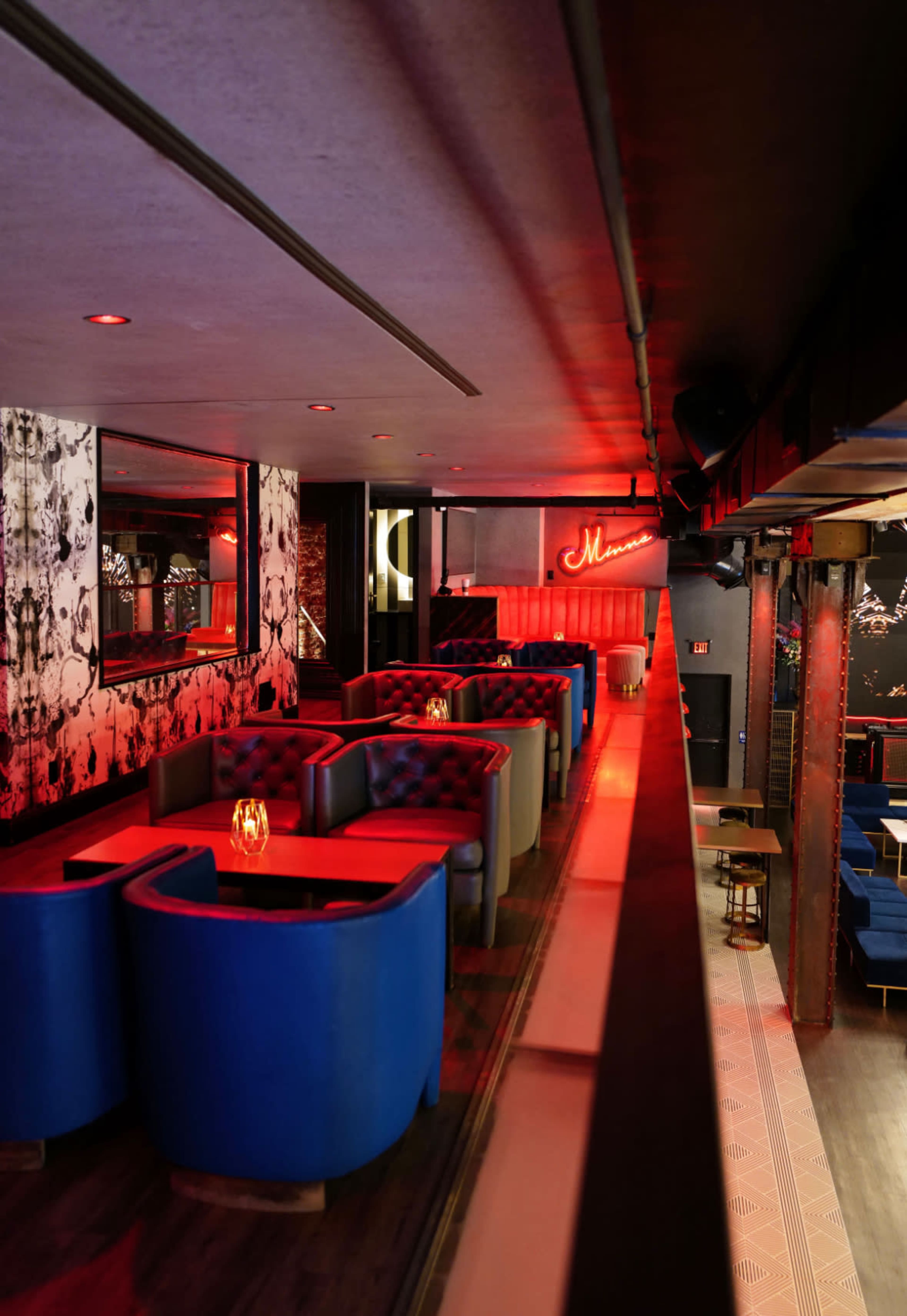 The image shows a dimly lit bar area featuring blue seating booths with ambient red lighting and decorative wall art.