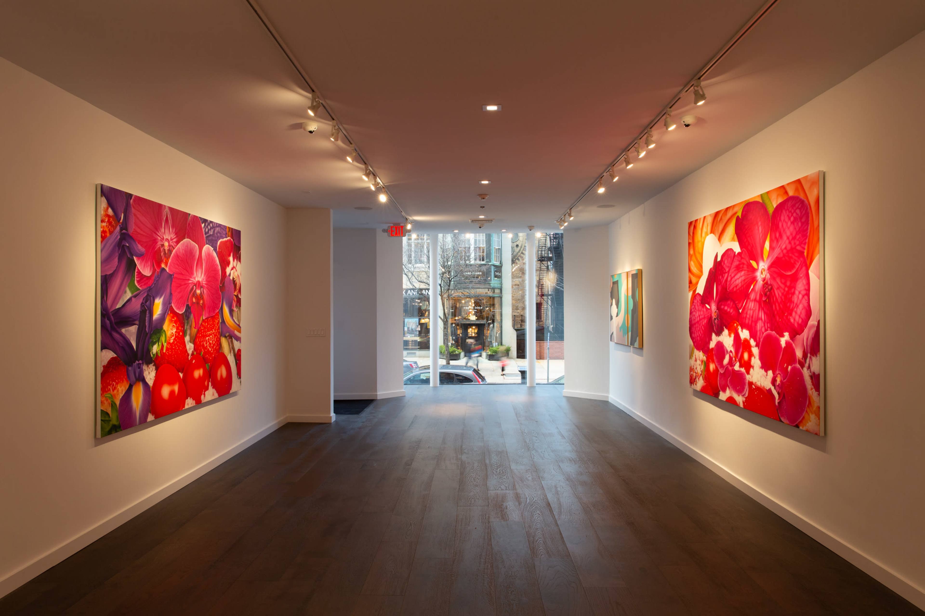 An art gallery with large floral paintings on two walls and a view of the street through a glass entrance.