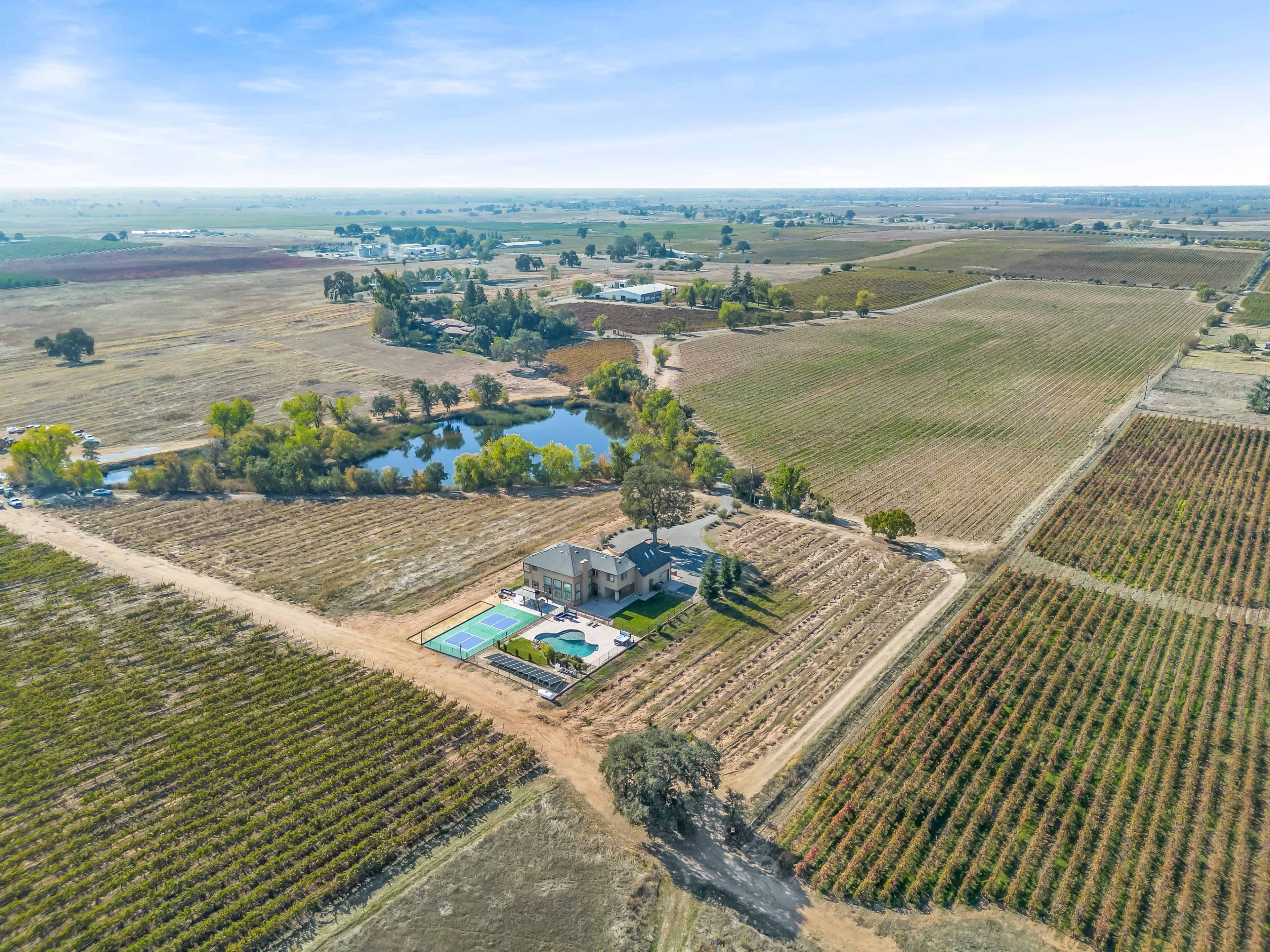 An aerial view of a large property featuring a house, swimming pool, and vineyard fields surrounding a small pond in a rural landscape.