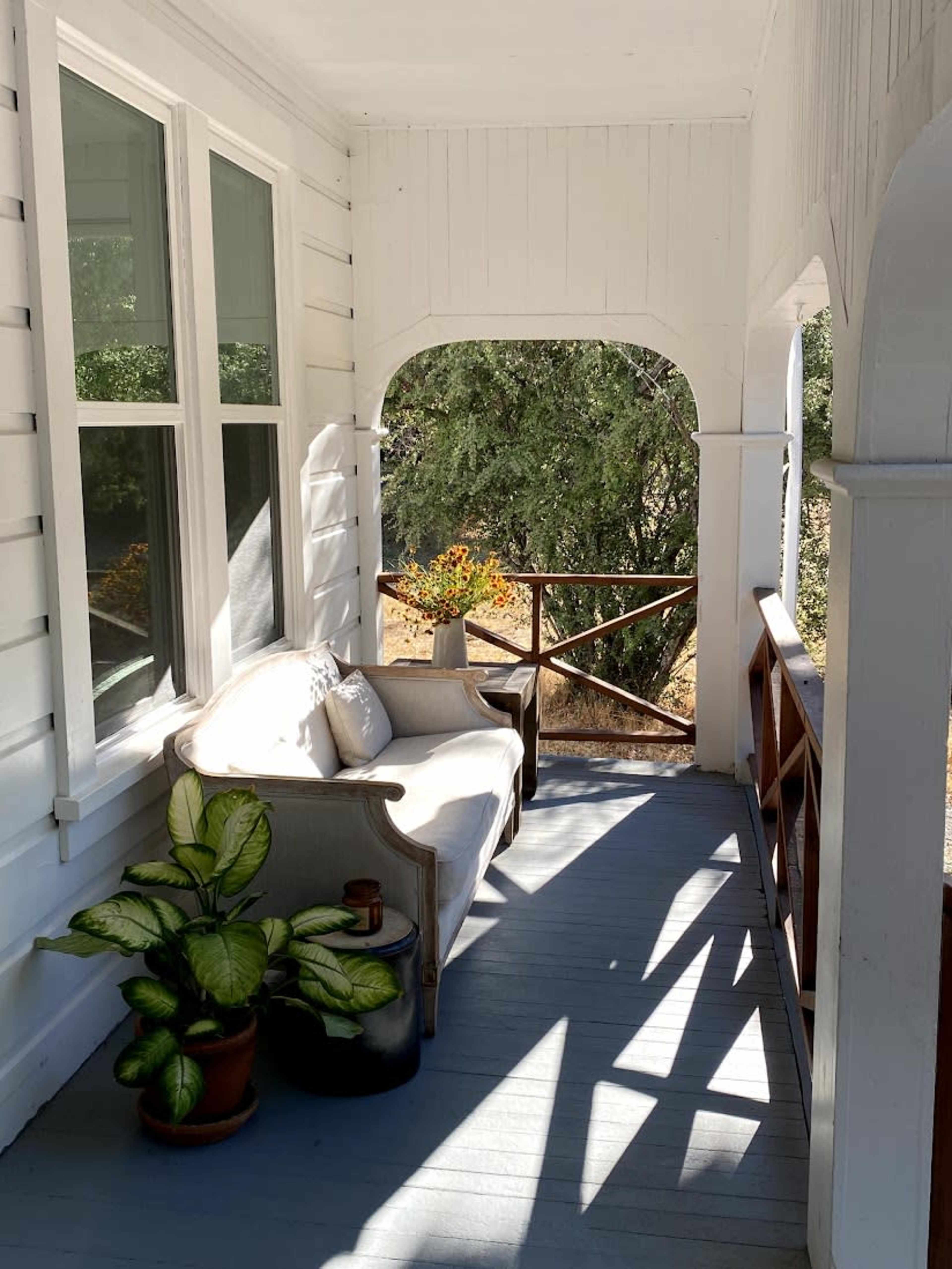 A porch area with a sofa, potted plant, and a view of trees through an arched opening.
