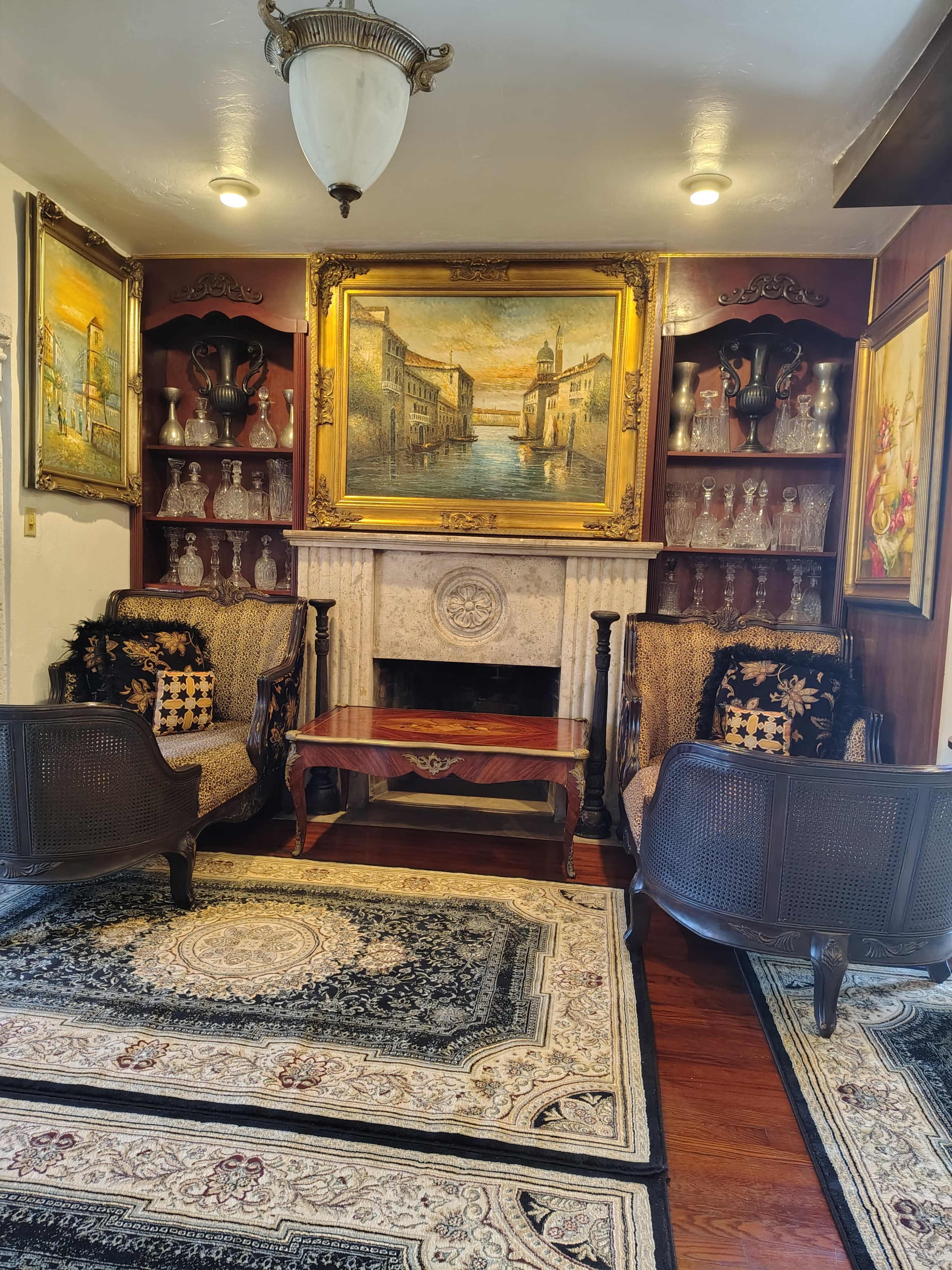 The image features a living room with two rattan chairs, a wooden coffee table, a decorative fireplace, and framed paintings on the walls.