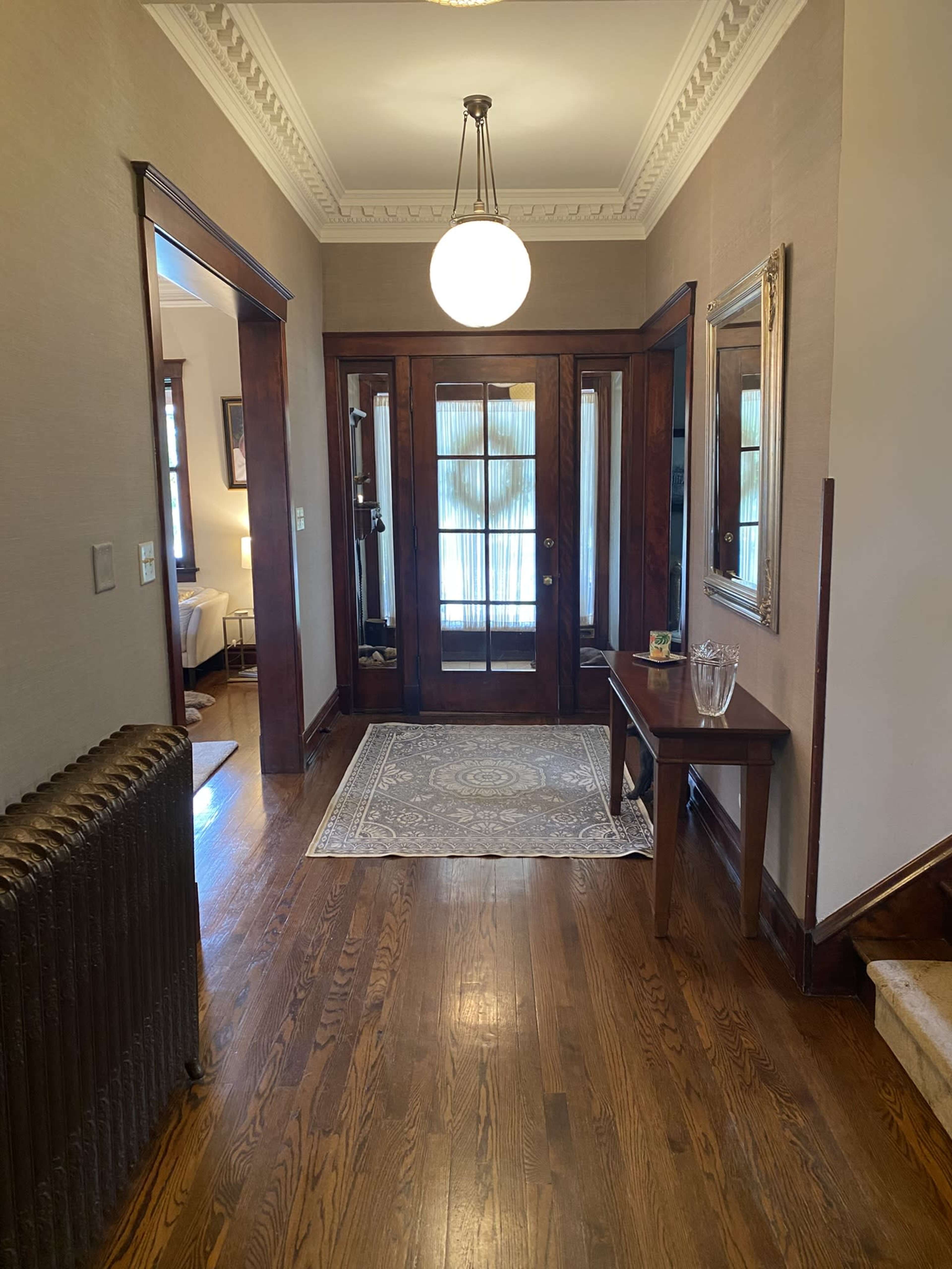 The image shows a hallway with wooden flooring, a decorative rug, and a round pendant light, flanked by doors and mirrors.