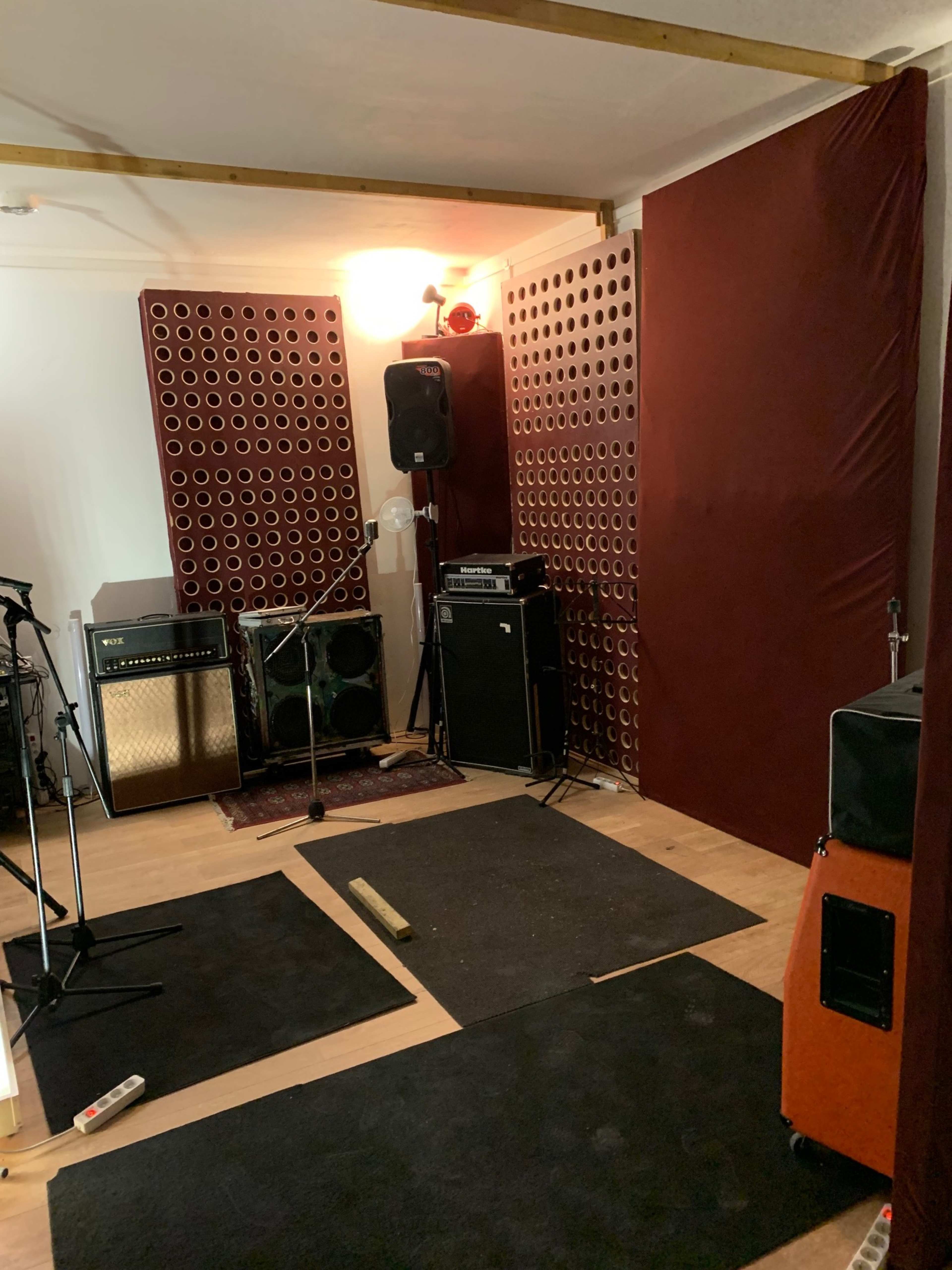 A music rehearsal space with sound-dampening panels, amplifiers, and microphones arranged around a wooden floor.