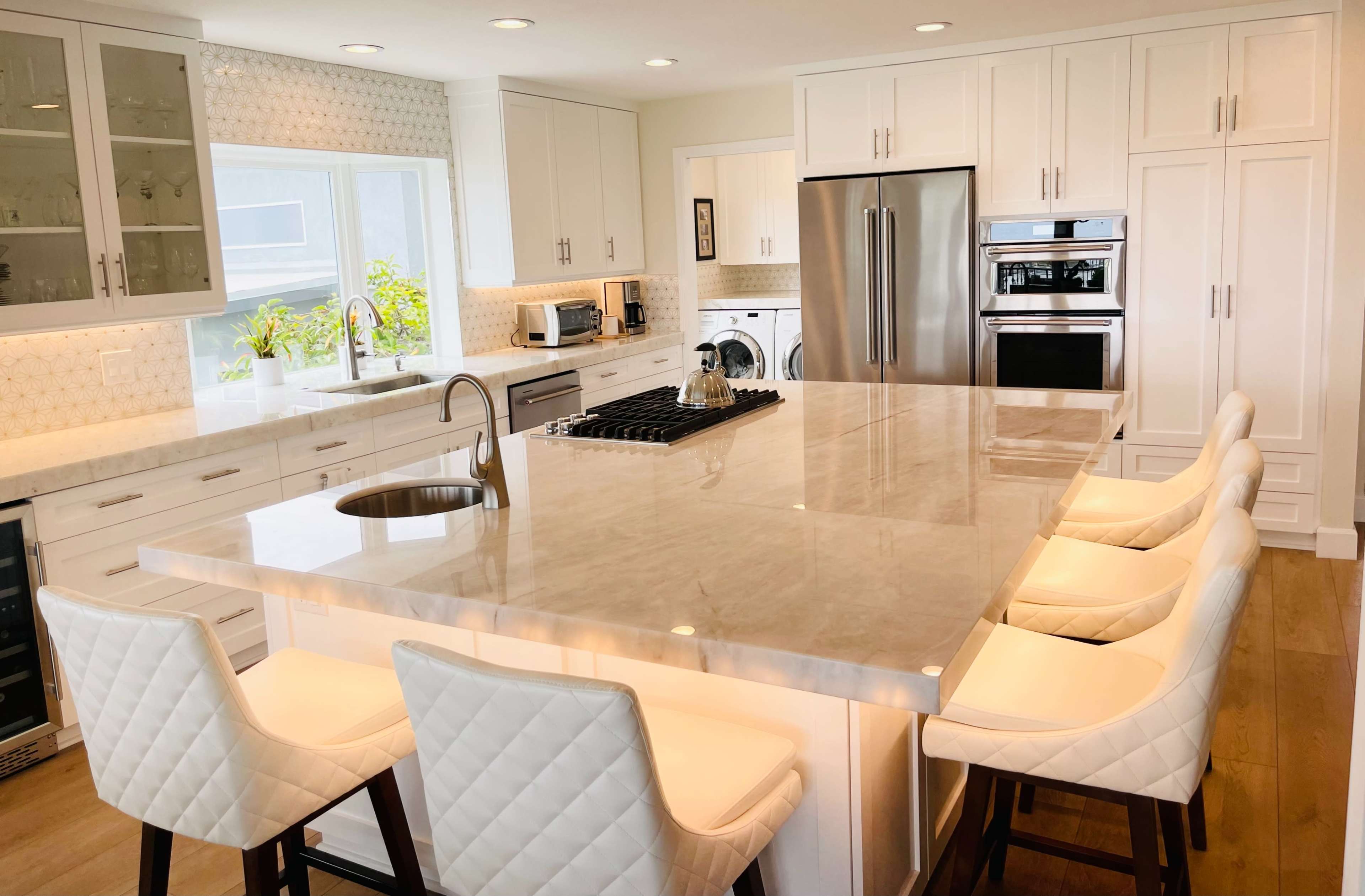 A modern kitchen featuring white cabinetry, a large marble island with bar seating, and stainless steel appliances.