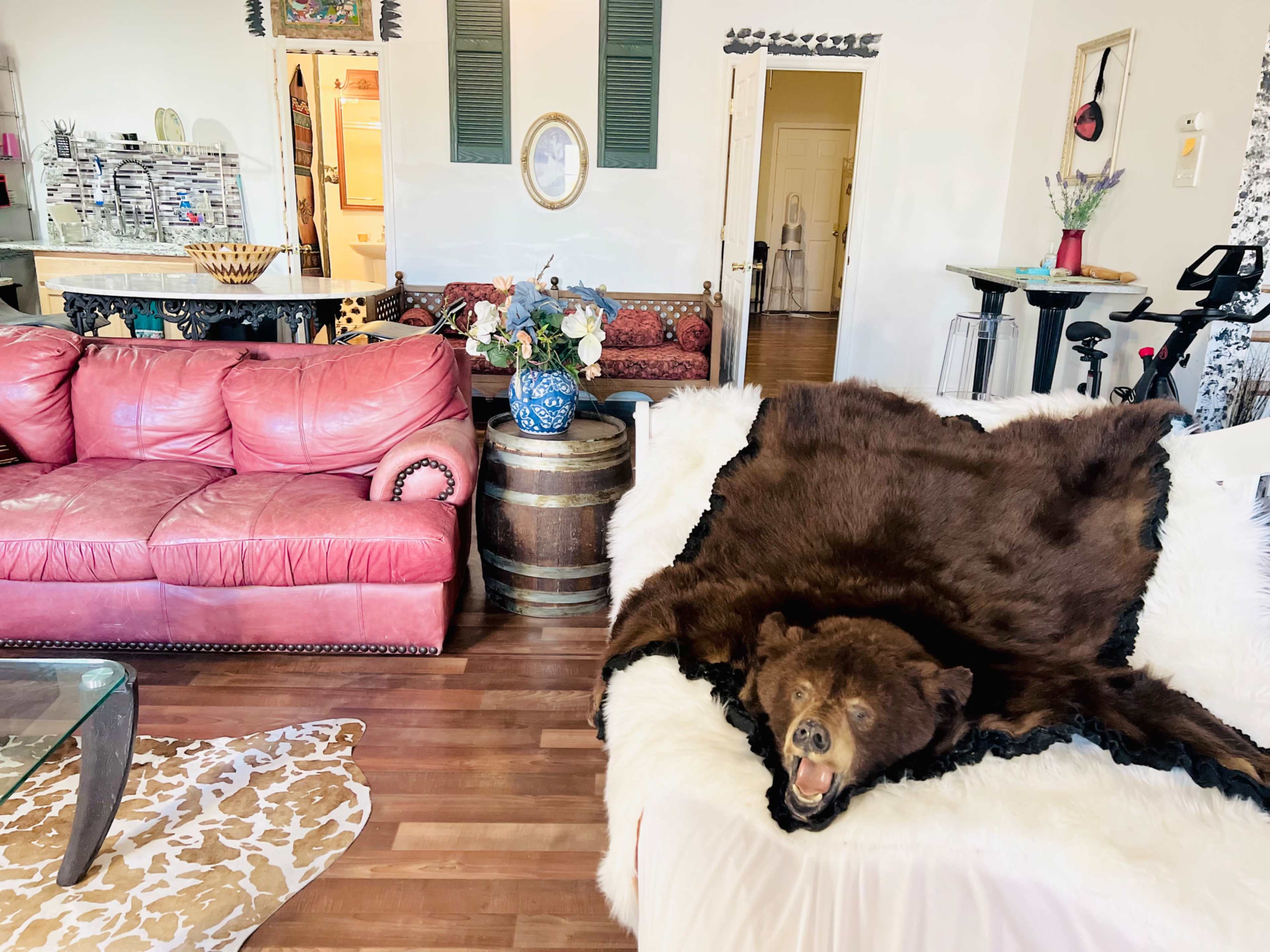 The living room features a pink leather sofa, a bear hide draped over a white couch, and a view into a kitchen area with various decorations.