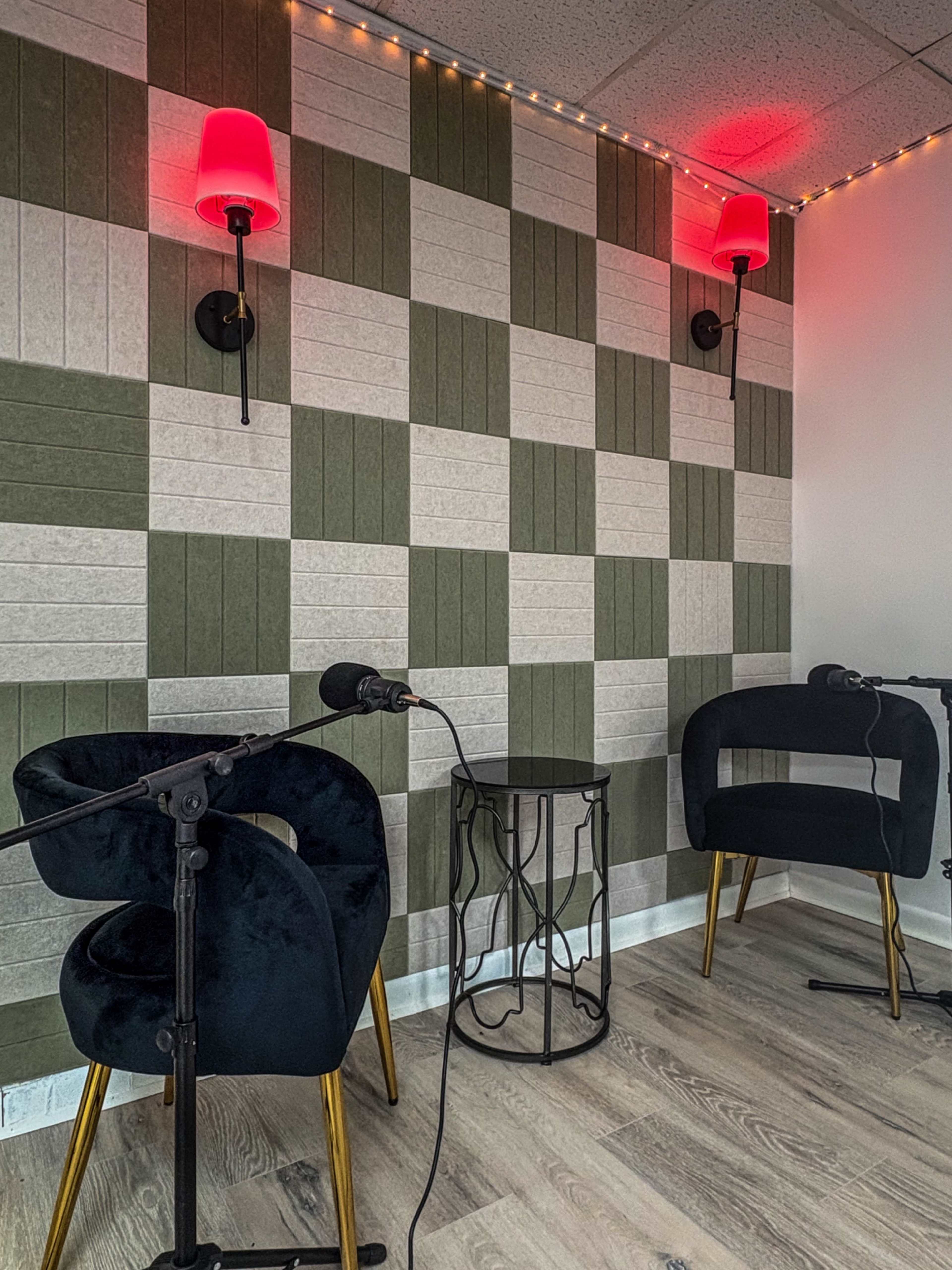 The image shows a small room with two black chairs, a small round table, and microphones, with a patterned wall featuring alternating green and light gray sections and red wall sconces.