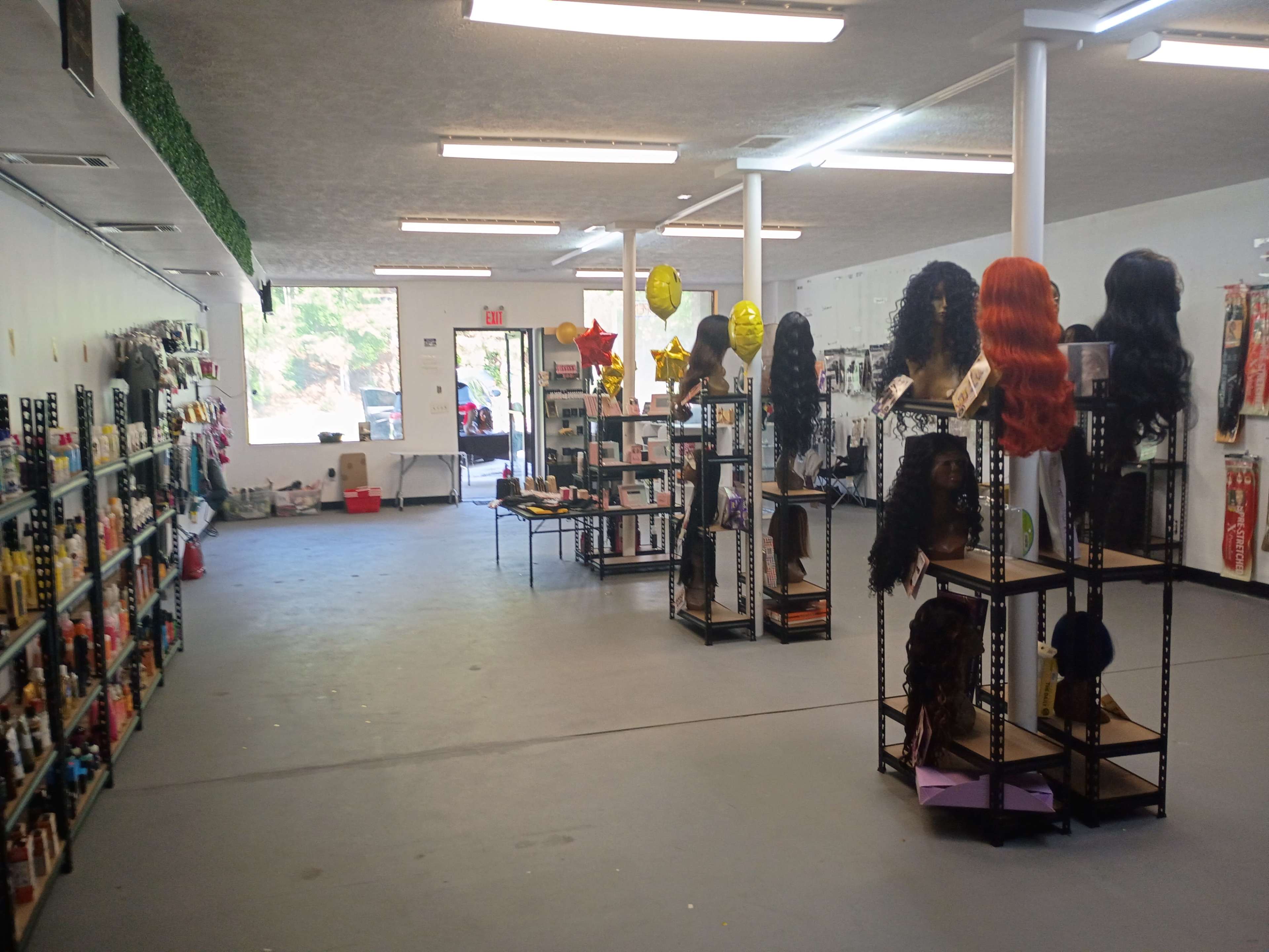The image shows the interior of a beauty supply store featuring shelves stocked with hair care products and a display of wigs on stands.