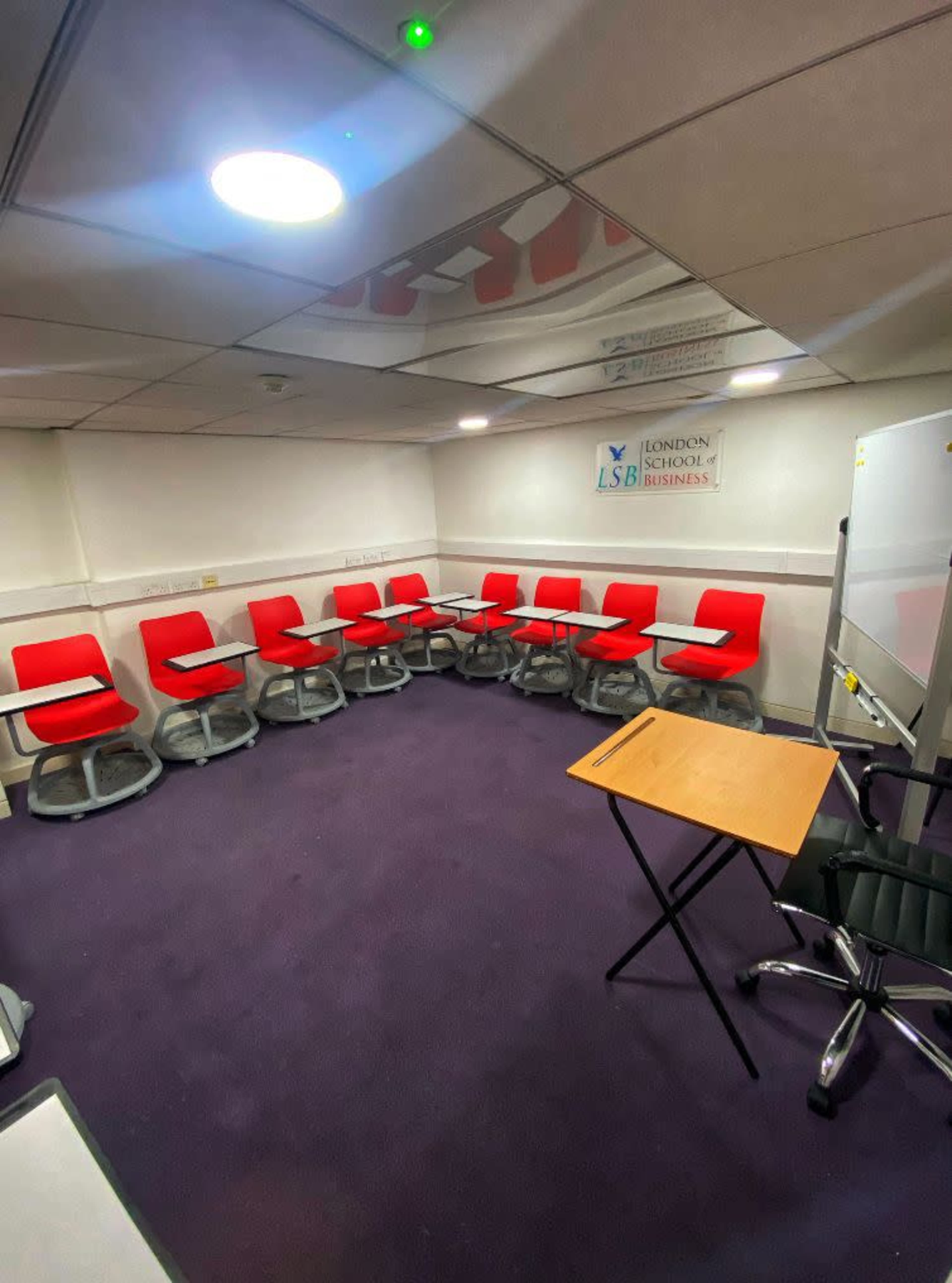 The image shows a small classroom or meeting room with circular seating arrangements featuring red chairs and a foldable table.