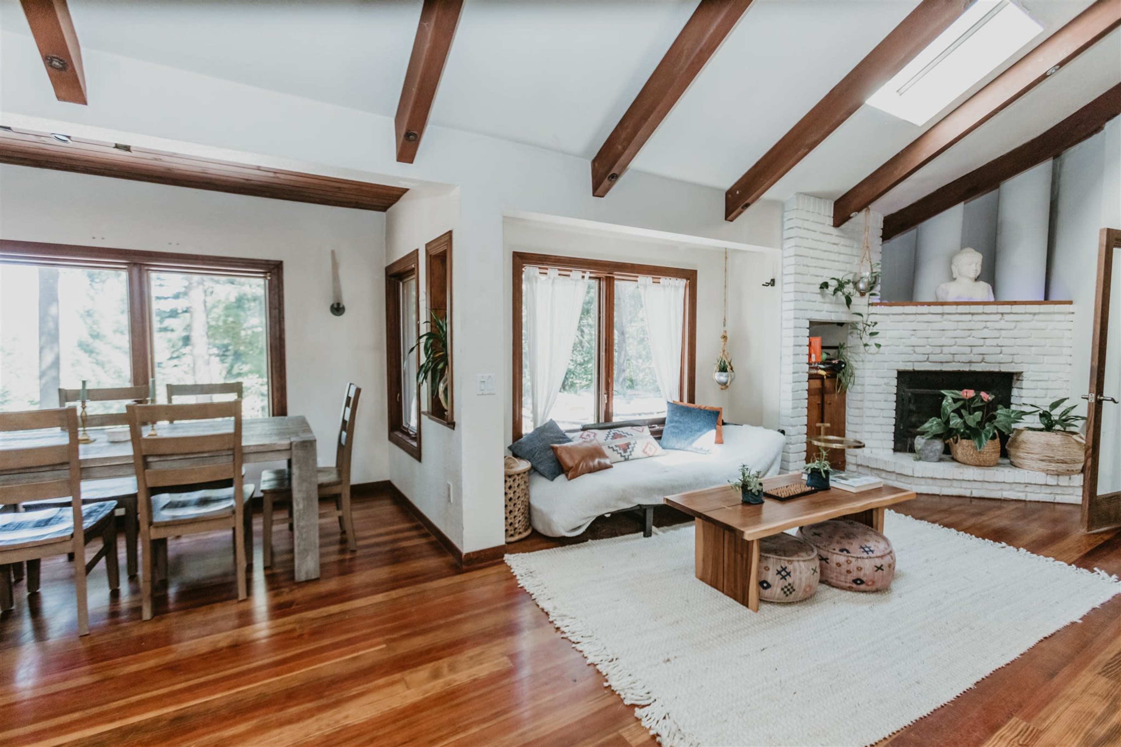 The image shows a living space featuring a dining area with a wooden table and chairs, a cozy seating area with a sofa, and a fireplace surrounded by a minimalist decor.