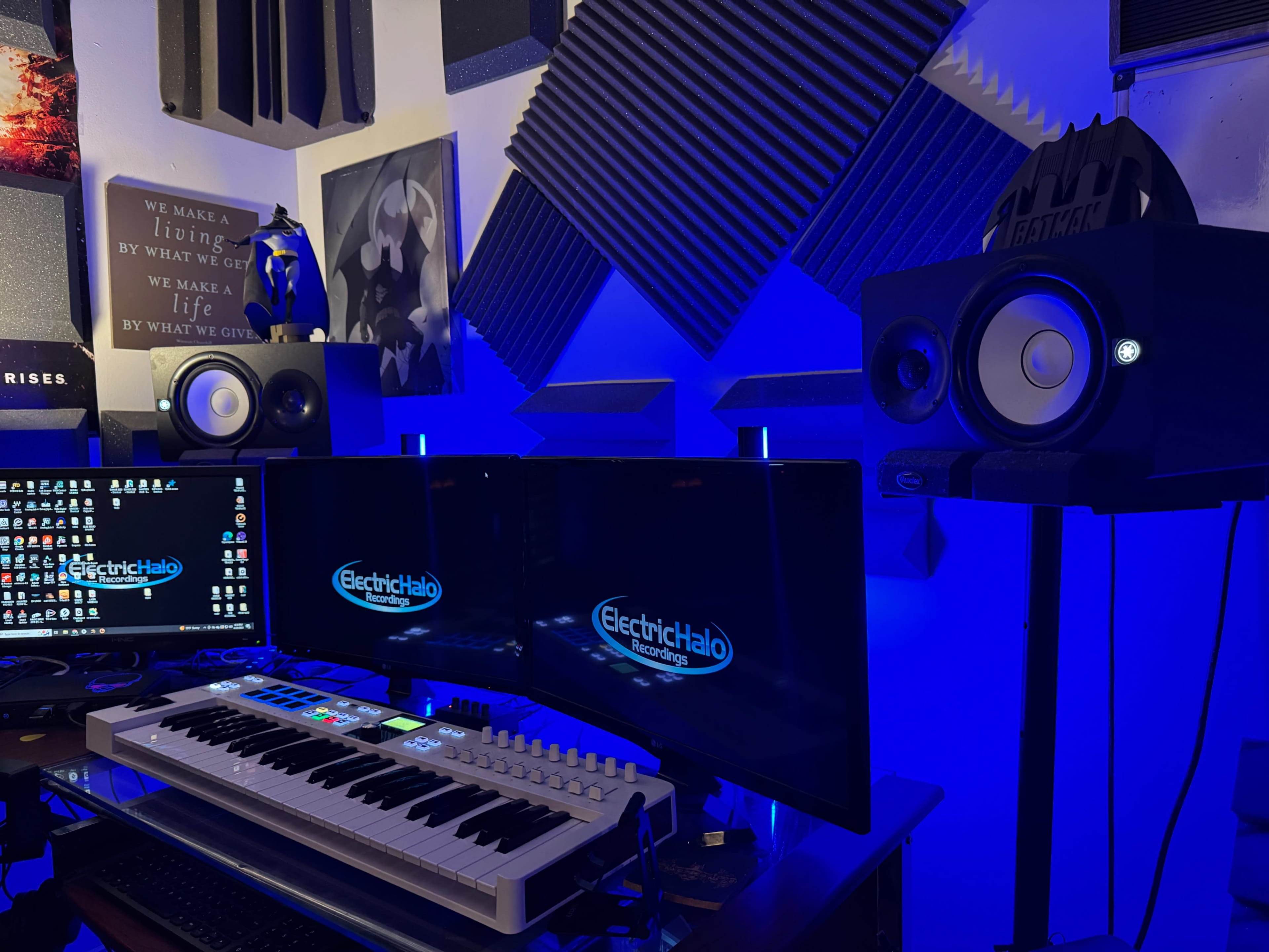 The image shows a music production setup featuring two monitors, a keyboard, and studio monitors in a room with soundproofing panels and blue lighting.