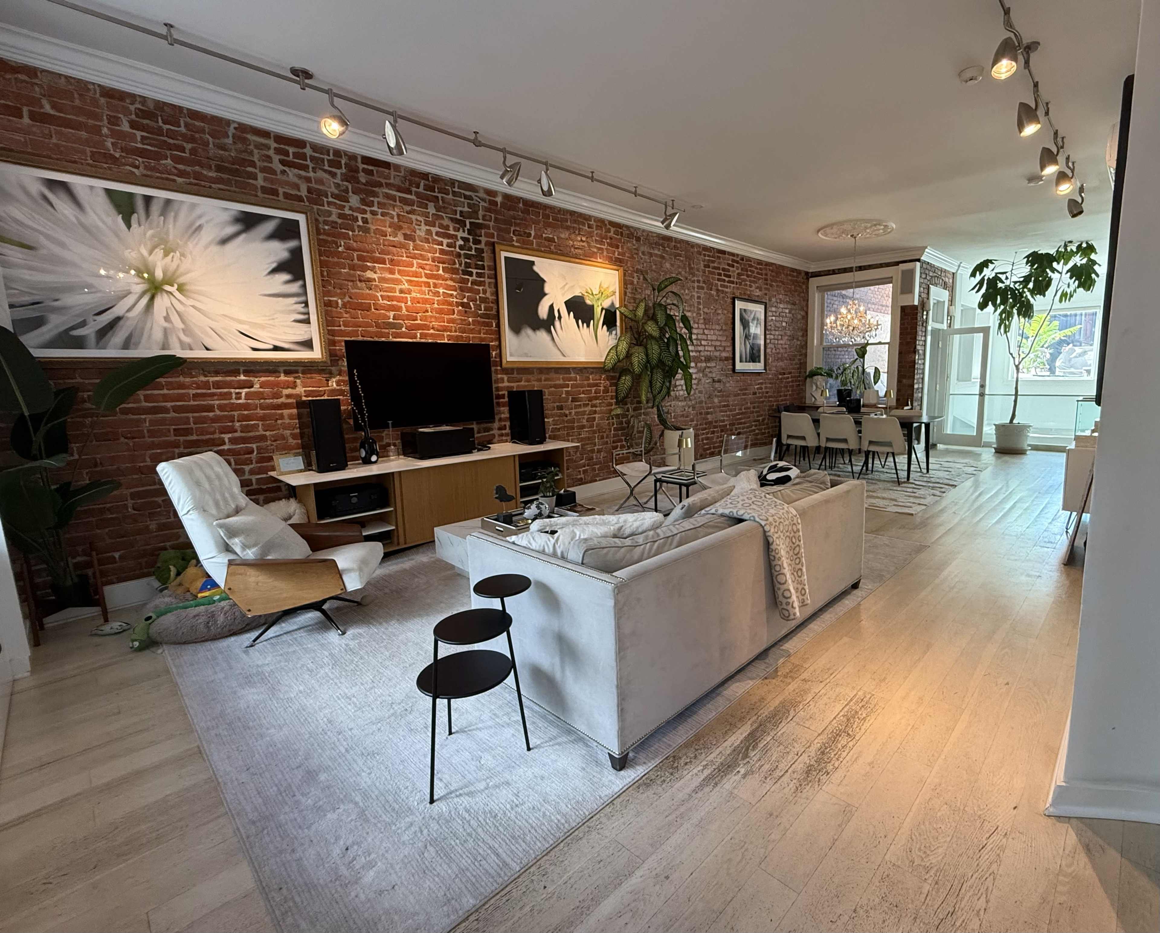 The image showcases a spacious living room with exposed brick walls, a large sofa, and a dining area featuring a table and chairs.