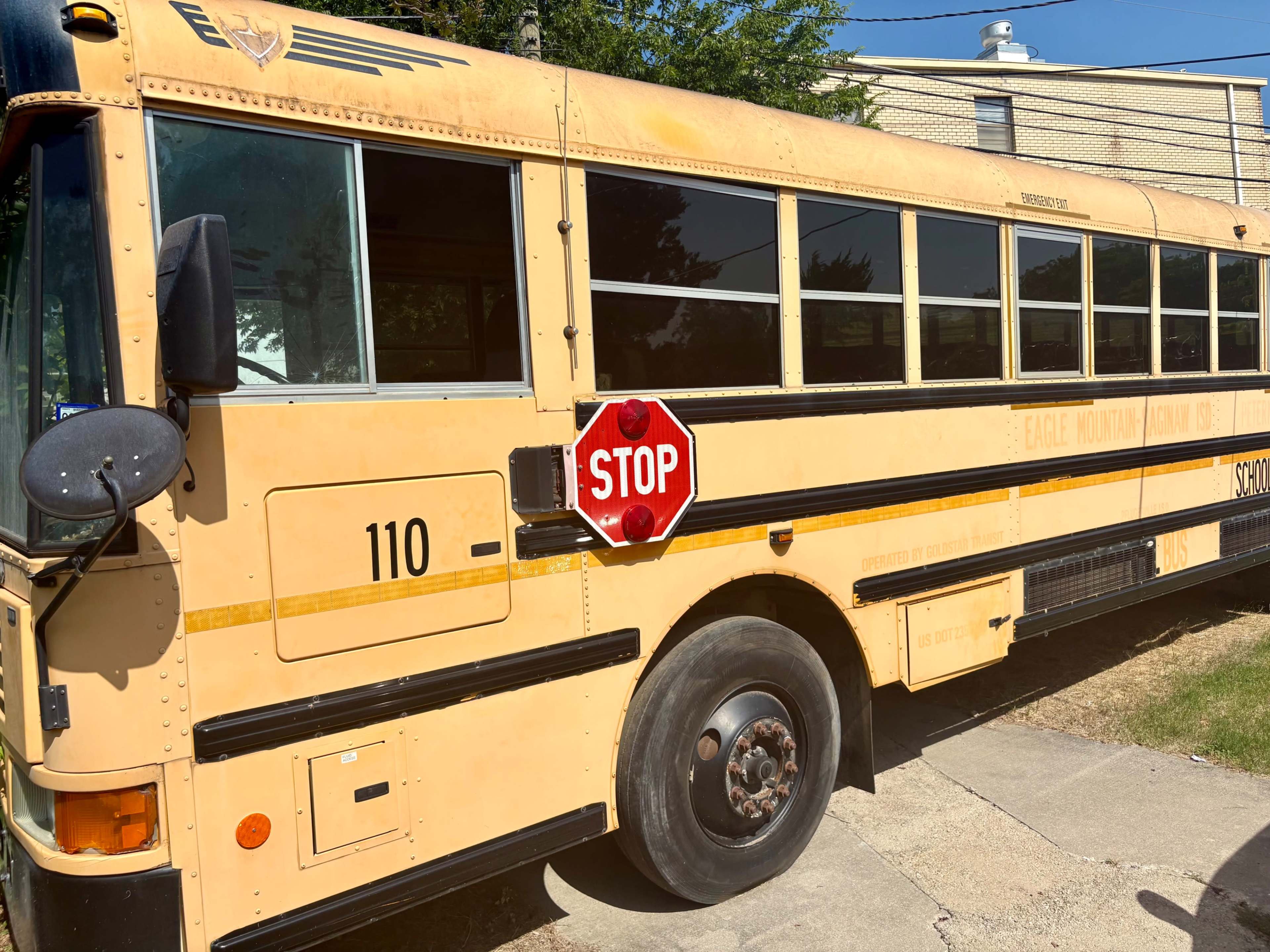 A yellow school bus with a red stop sign is parked beside a concrete driveway.