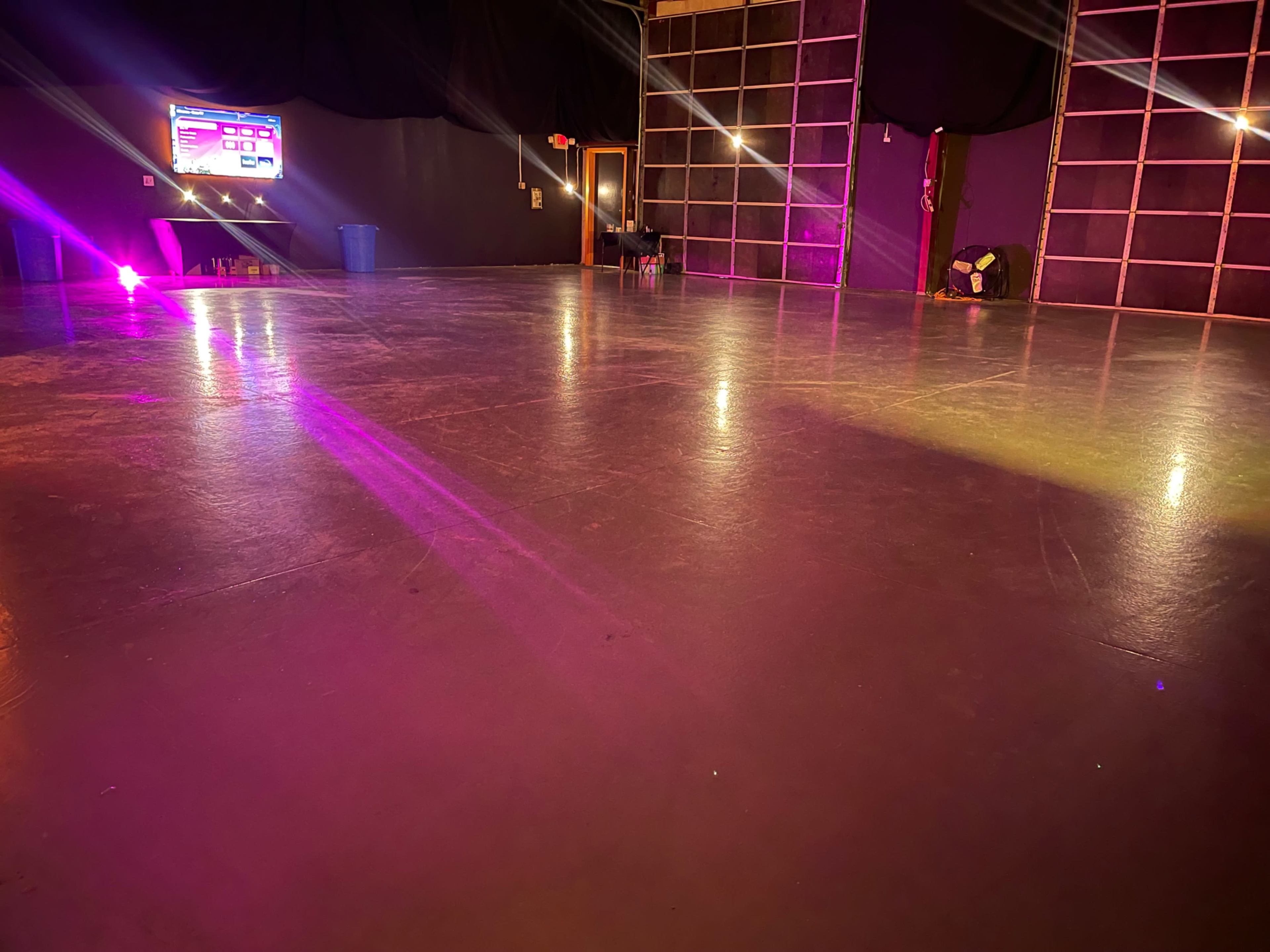 A dance studio with a polished floor, illuminated by colored lights, and a digital display visible in the background.