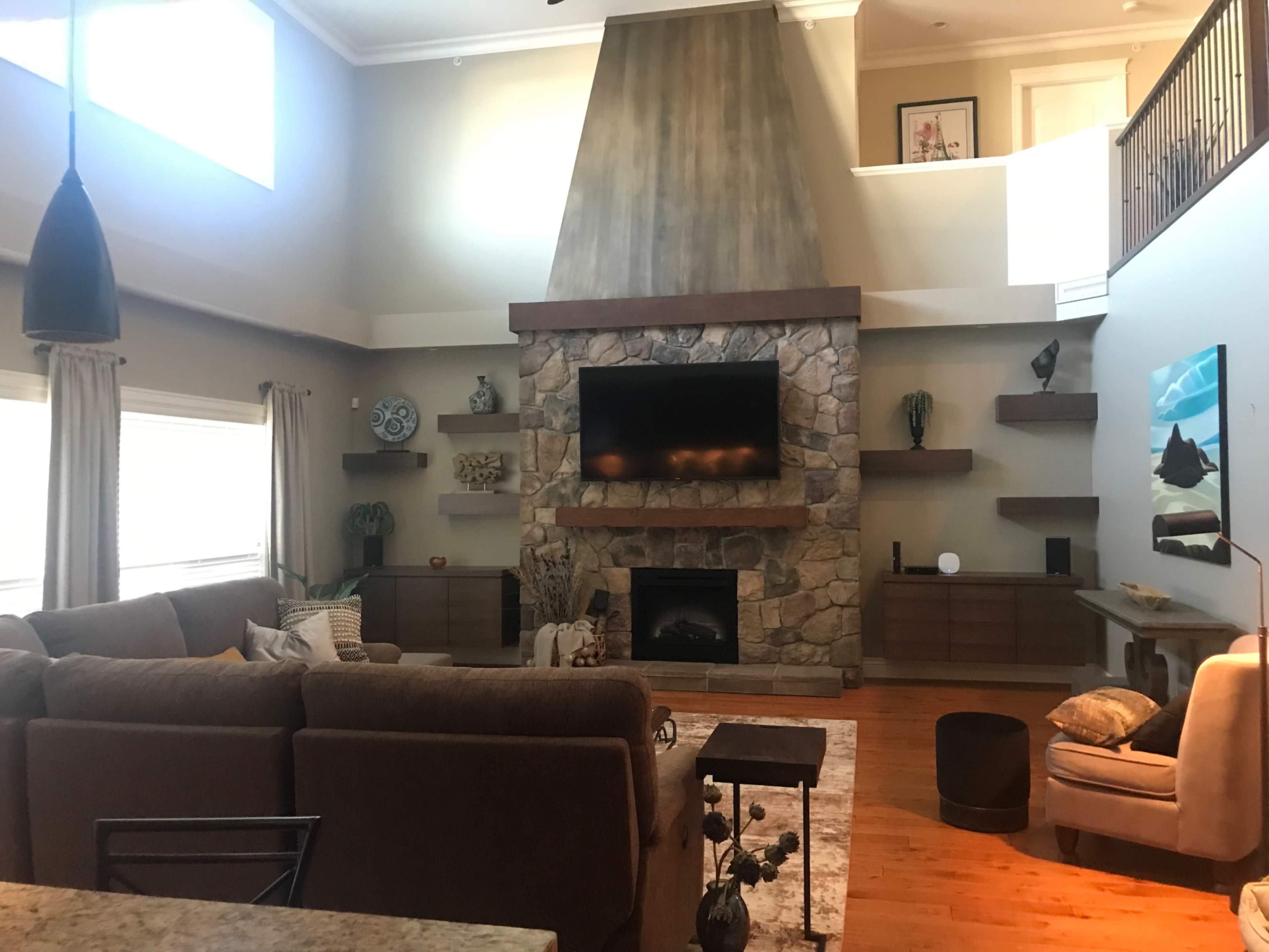 A spacious living room with a stone fireplace, a large flat-screen TV mounted above it, and a sectional sofa facing the fireplace.