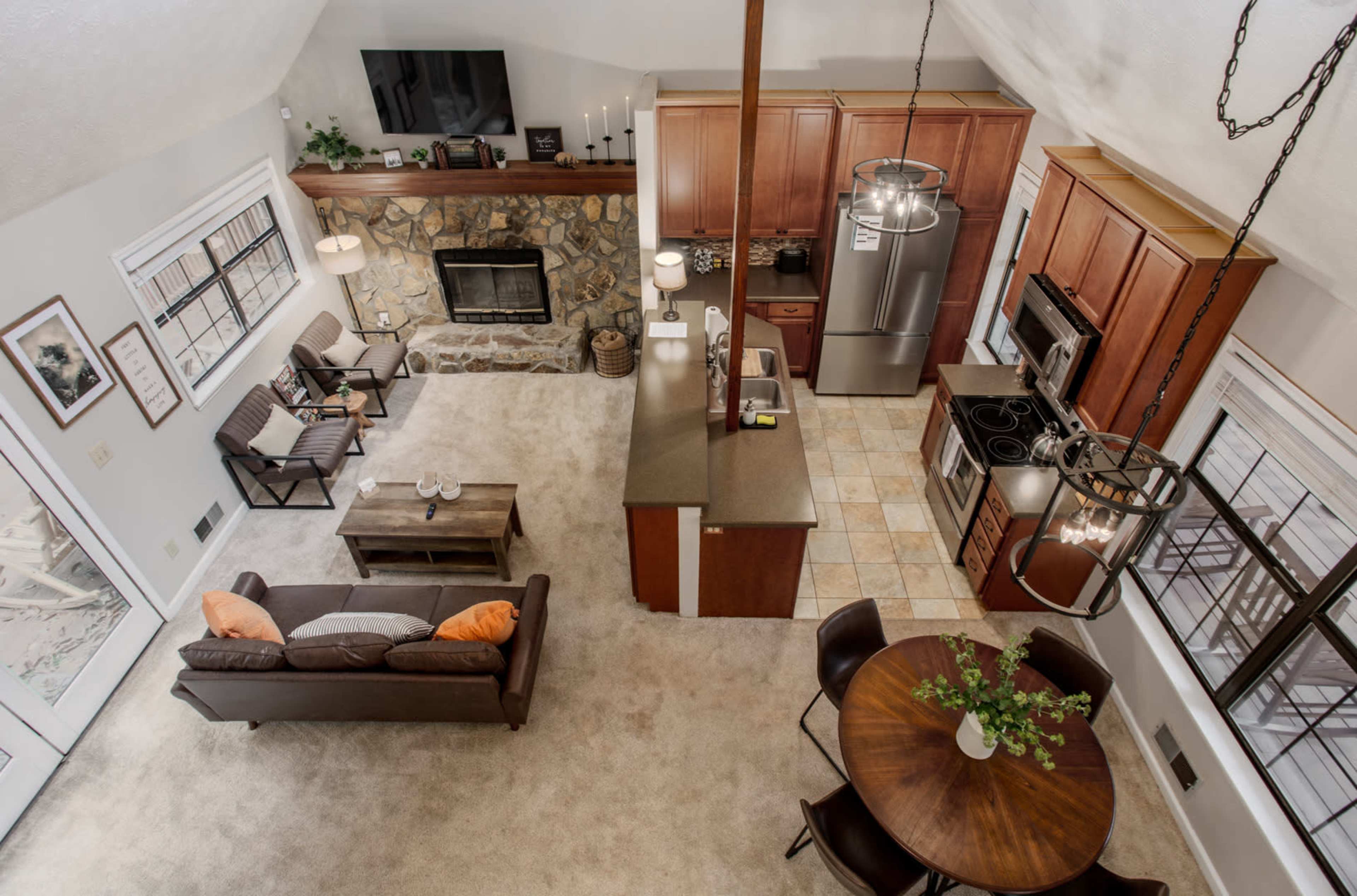 An open-concept living area and kitchen with a stone fireplace, modern appliances, and a dining table.