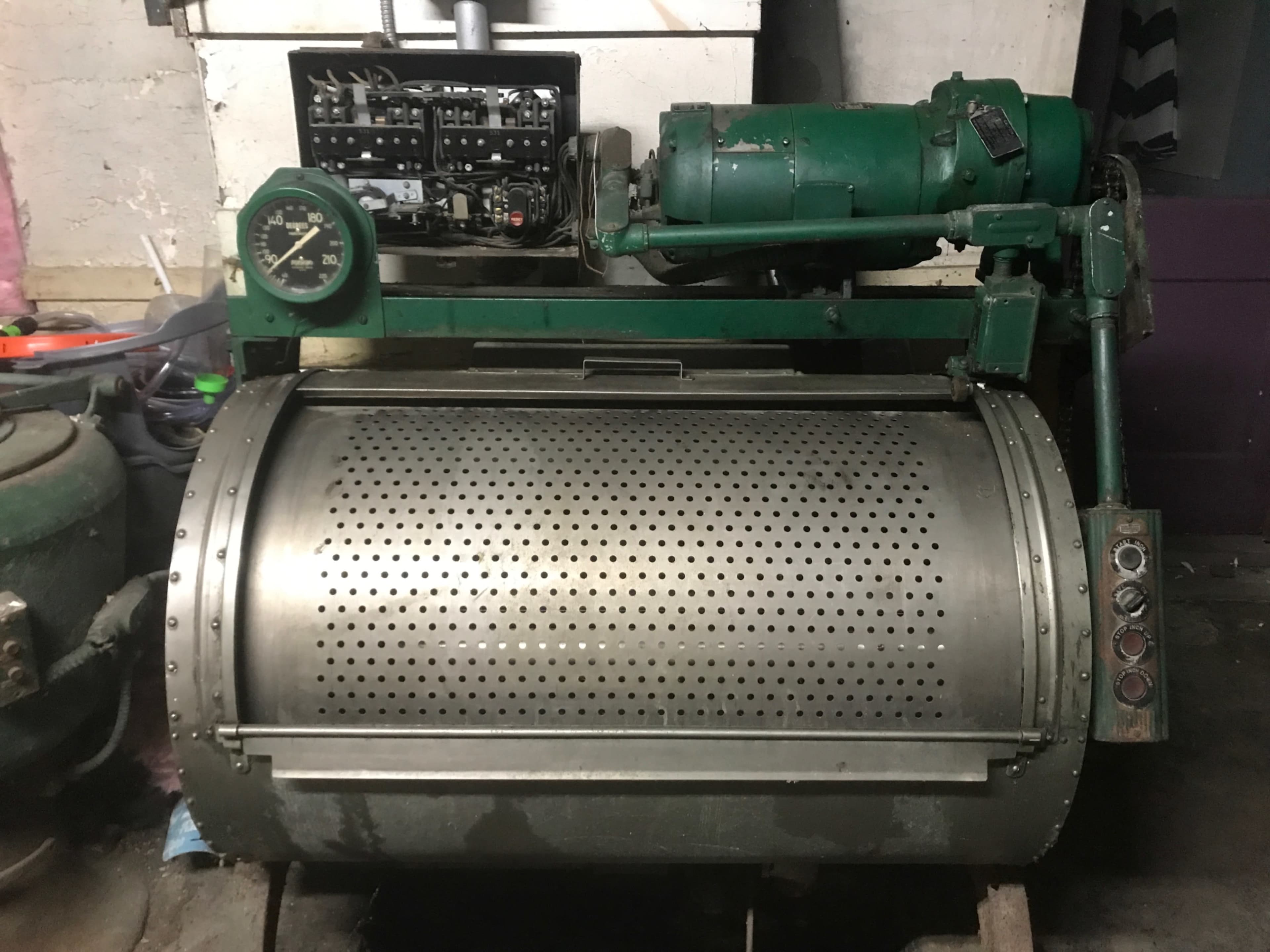 A large, green industrial machine with a perforated cylindrical drum and a motor mounted above it.