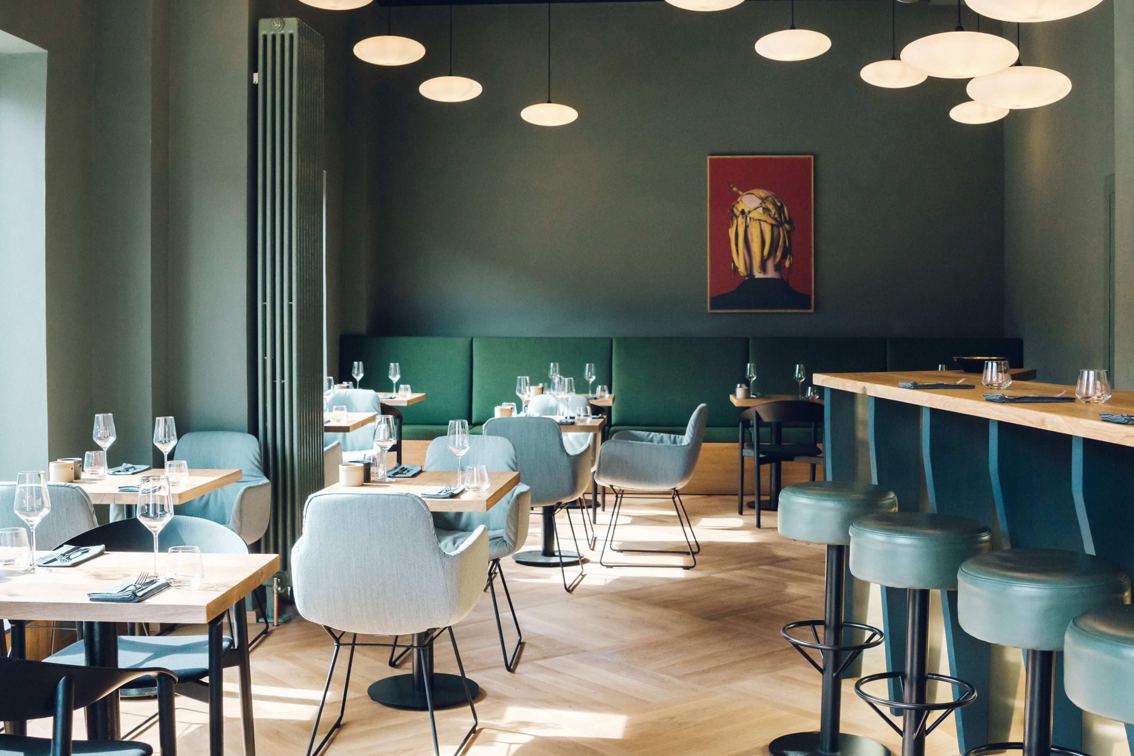 The image shows a modern restaurant interior with a combination of dining tables, chairs, and a bar area featuring round pendant lights and green walls.