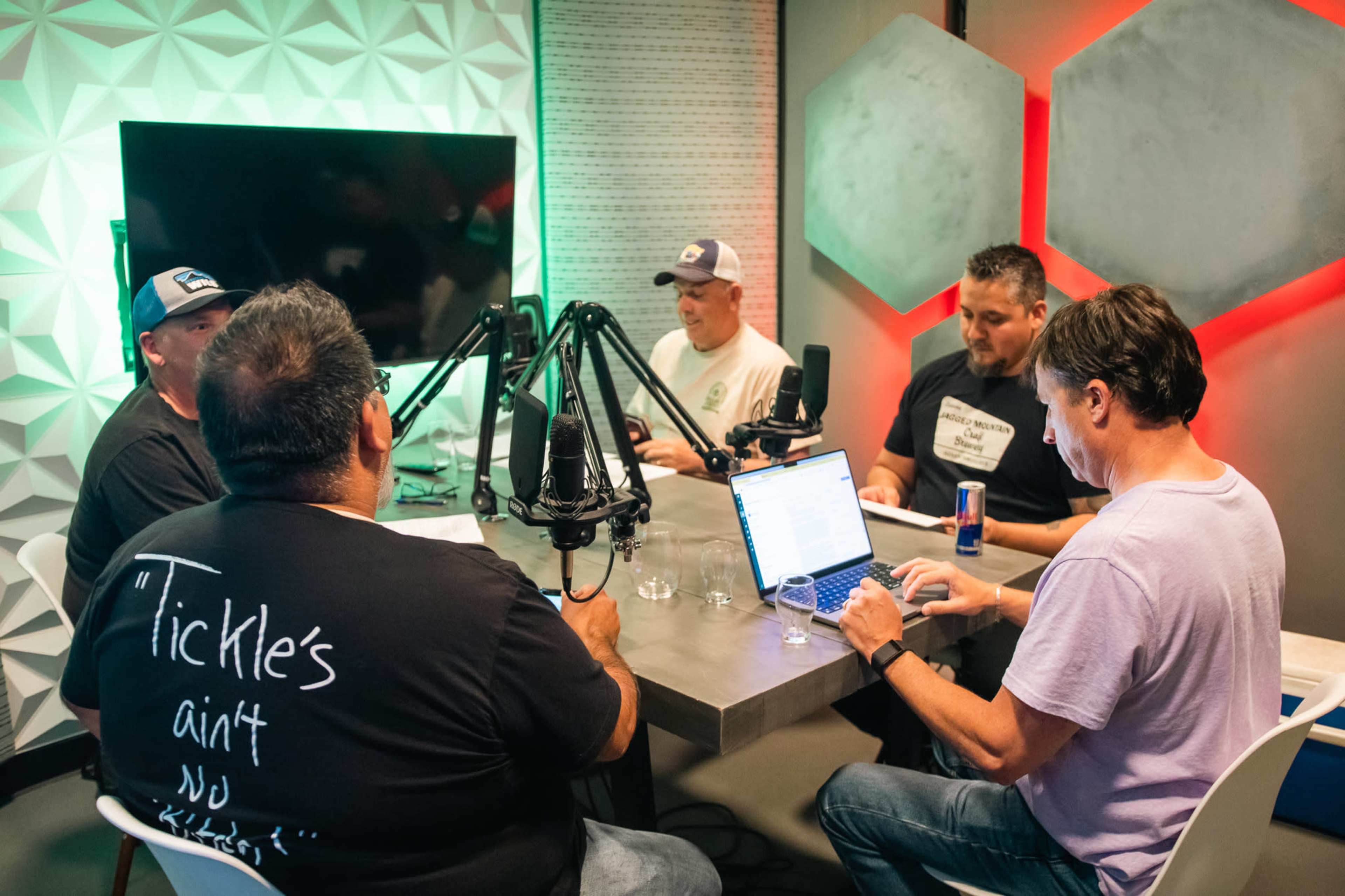 Five people are gathered around a table equipped with microphones and laptops in a modern workspace.