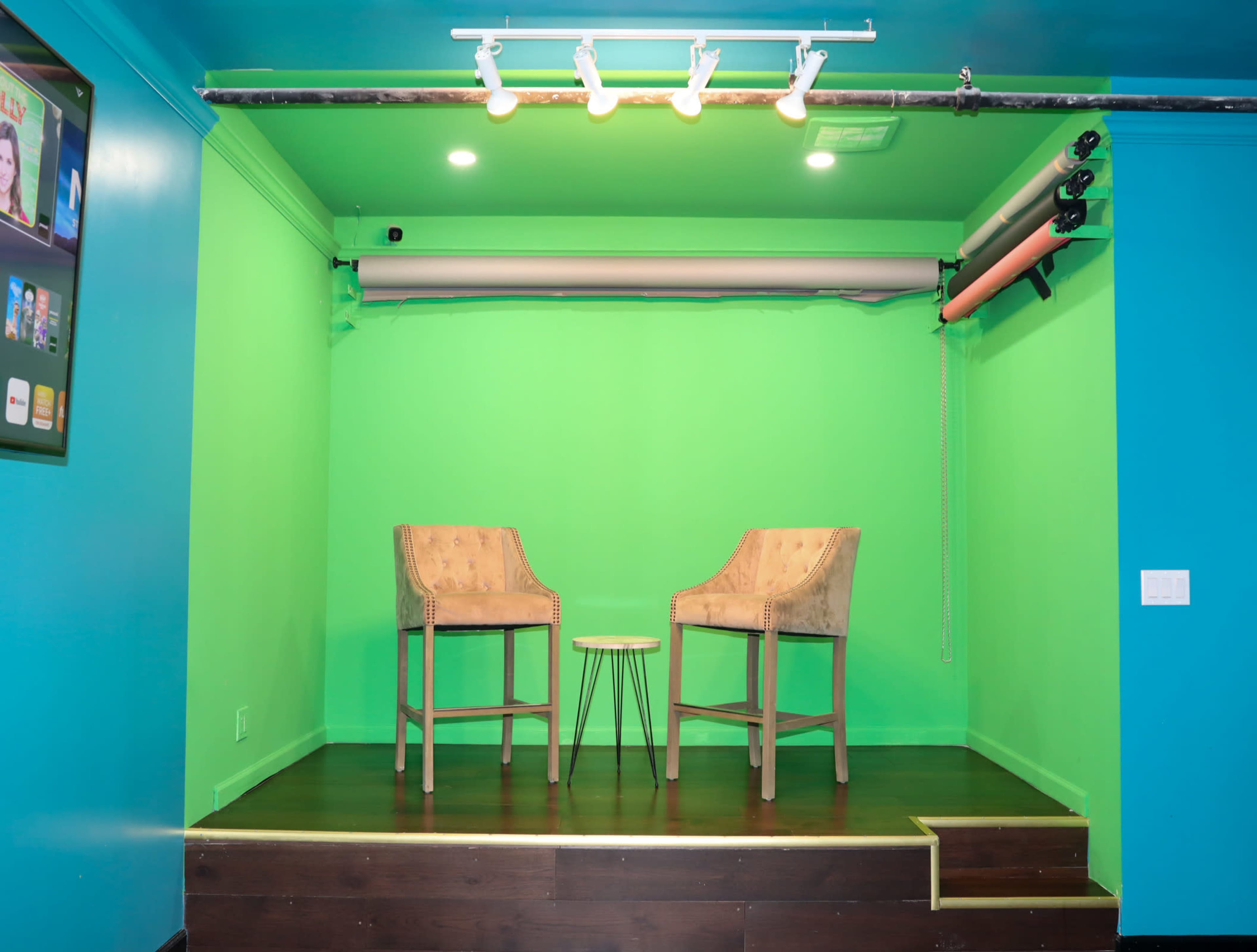 A small stage with two chairs and a table is set against a bright green backdrop.