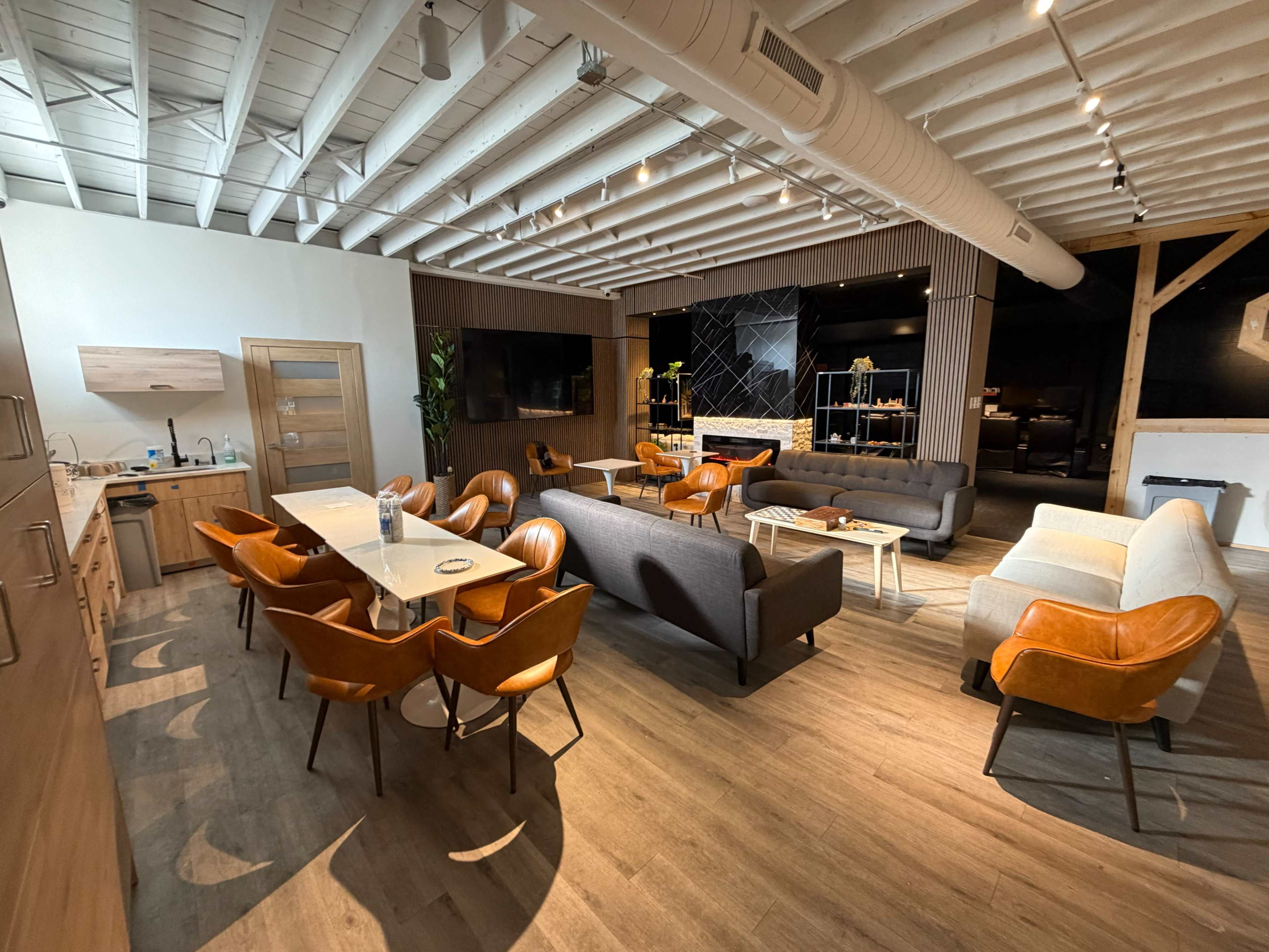 The image shows a modern interior space featuring a dining area with orange chairs, a lounge area with gray and orange sofas, and a kitchen area with wooden cabinetry.