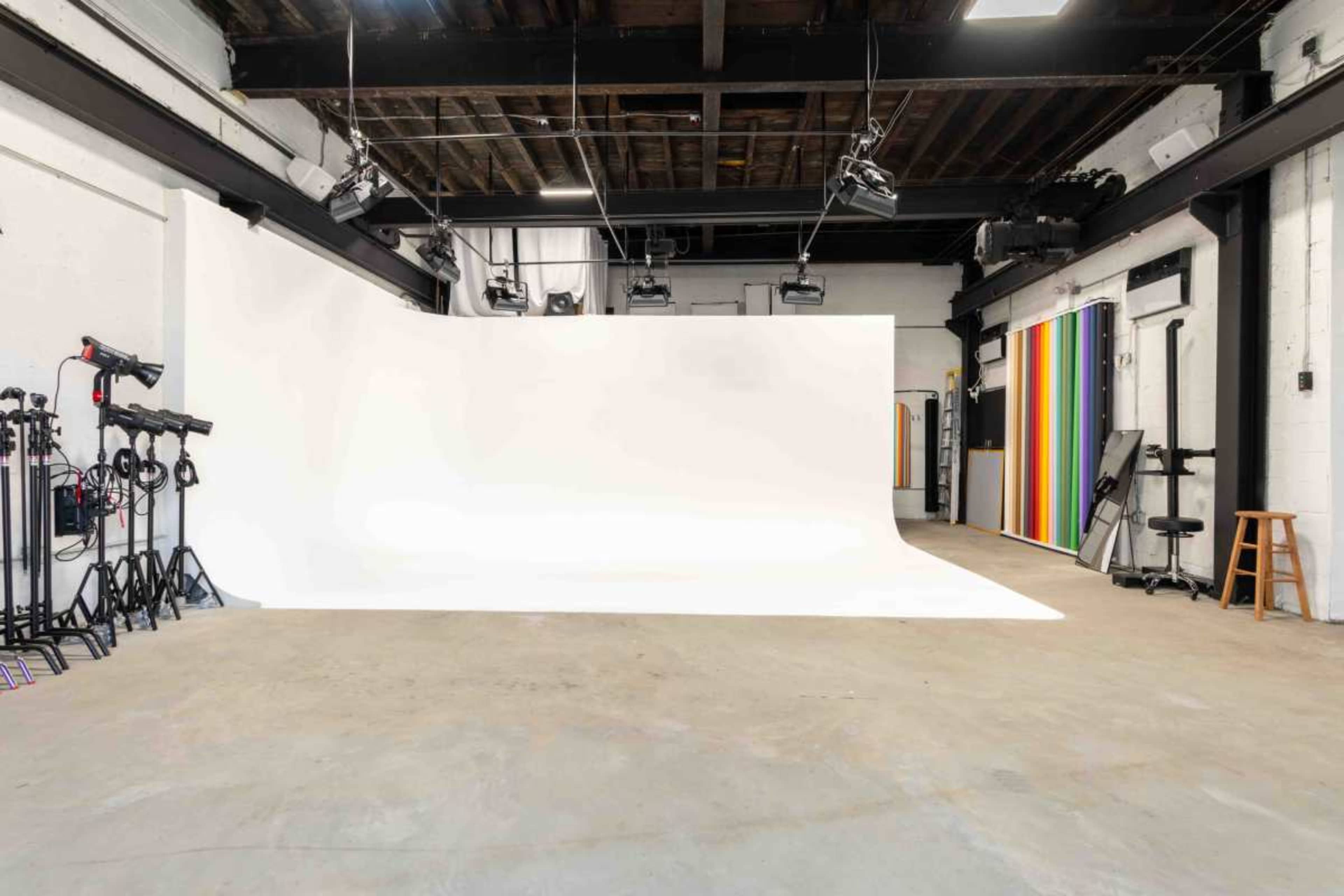 The image shows a spacious photography studio with a white backdrop and various lighting equipment arranged on the left side.
