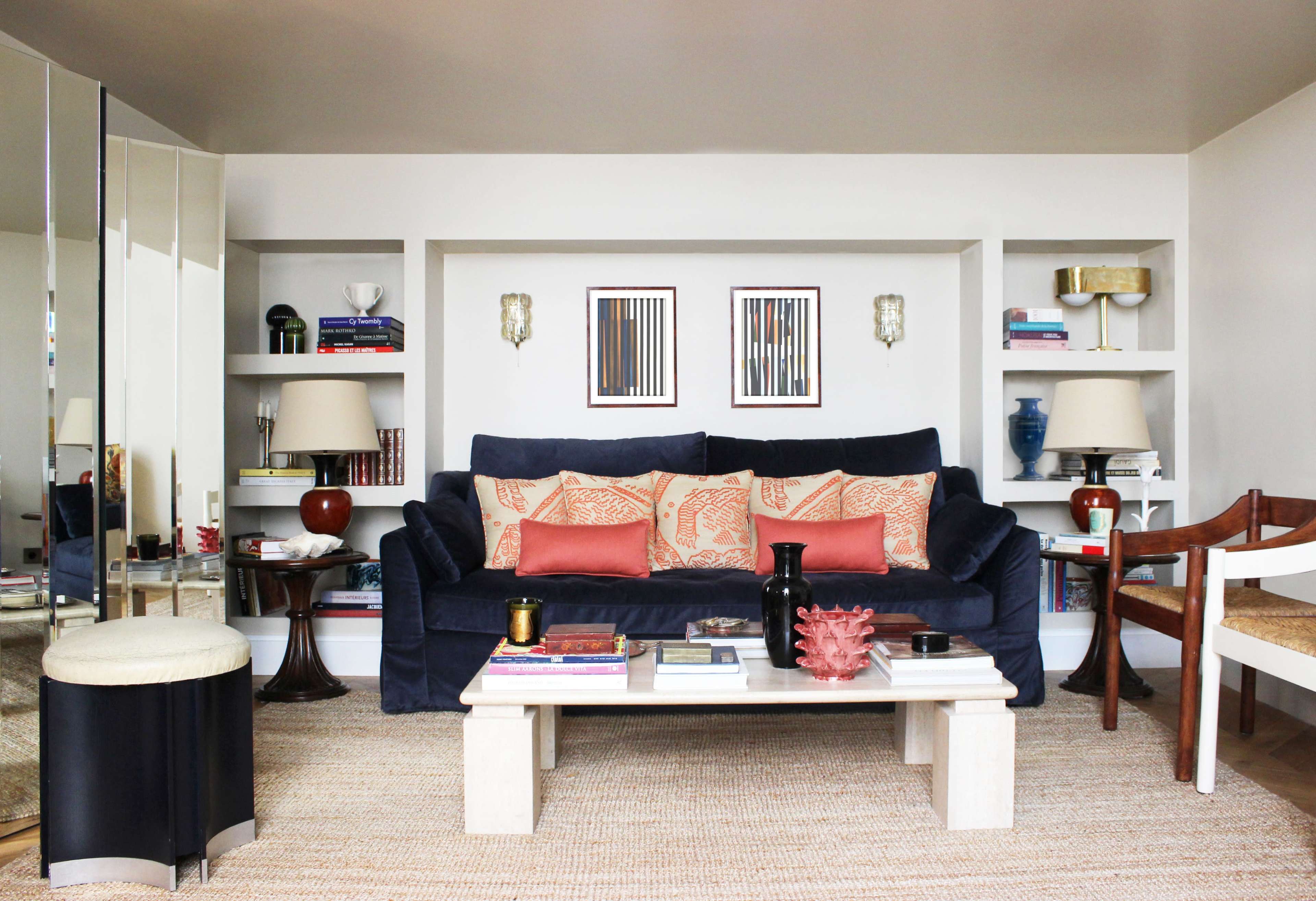 The image shows a stylish living room featuring a navy blue couch with patterned cushions, a coffee table, and shelves filled with books and decorative items.