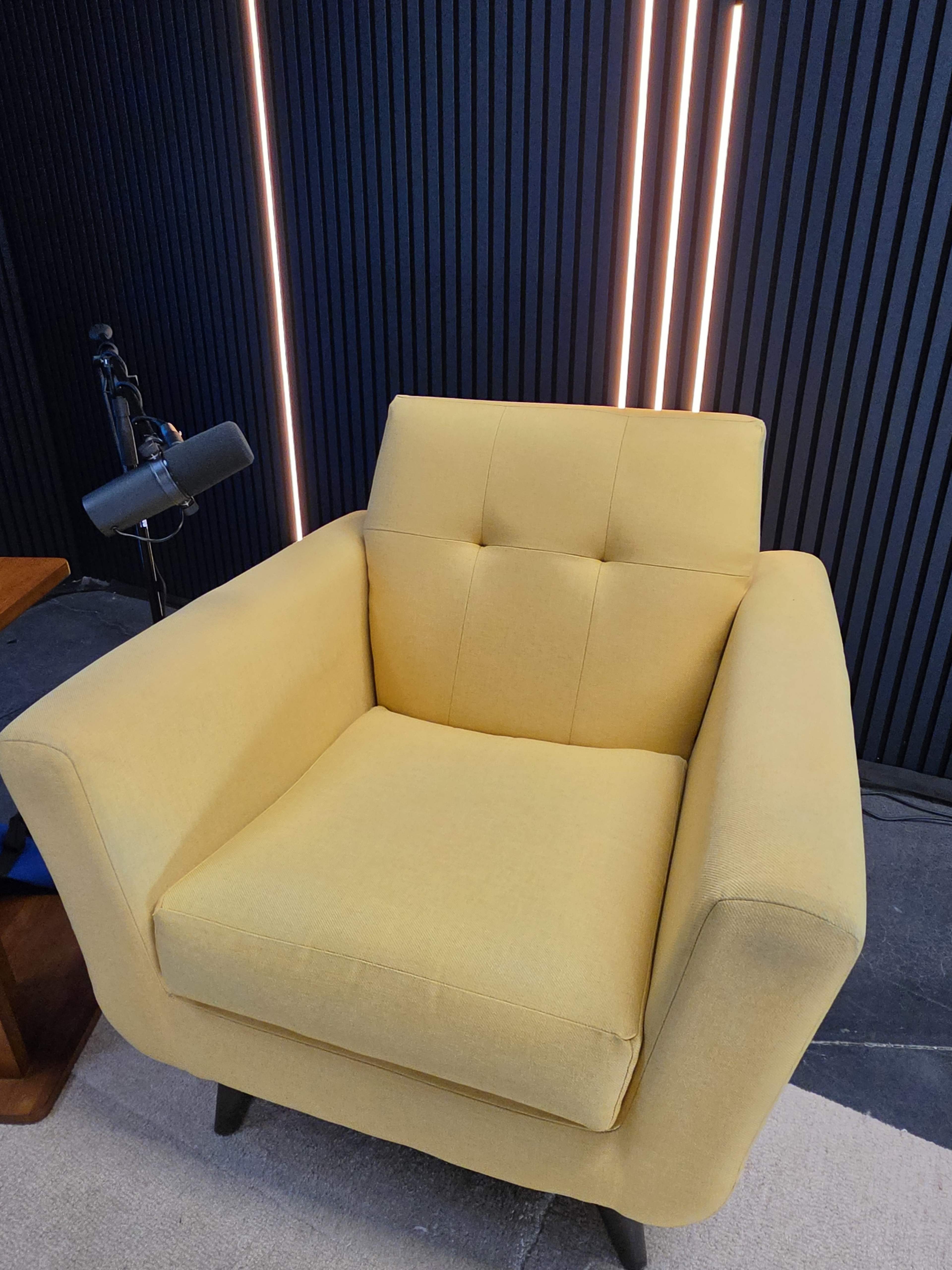 The image shows a yellow armchair positioned against a black paneled wall with vertical light strips.