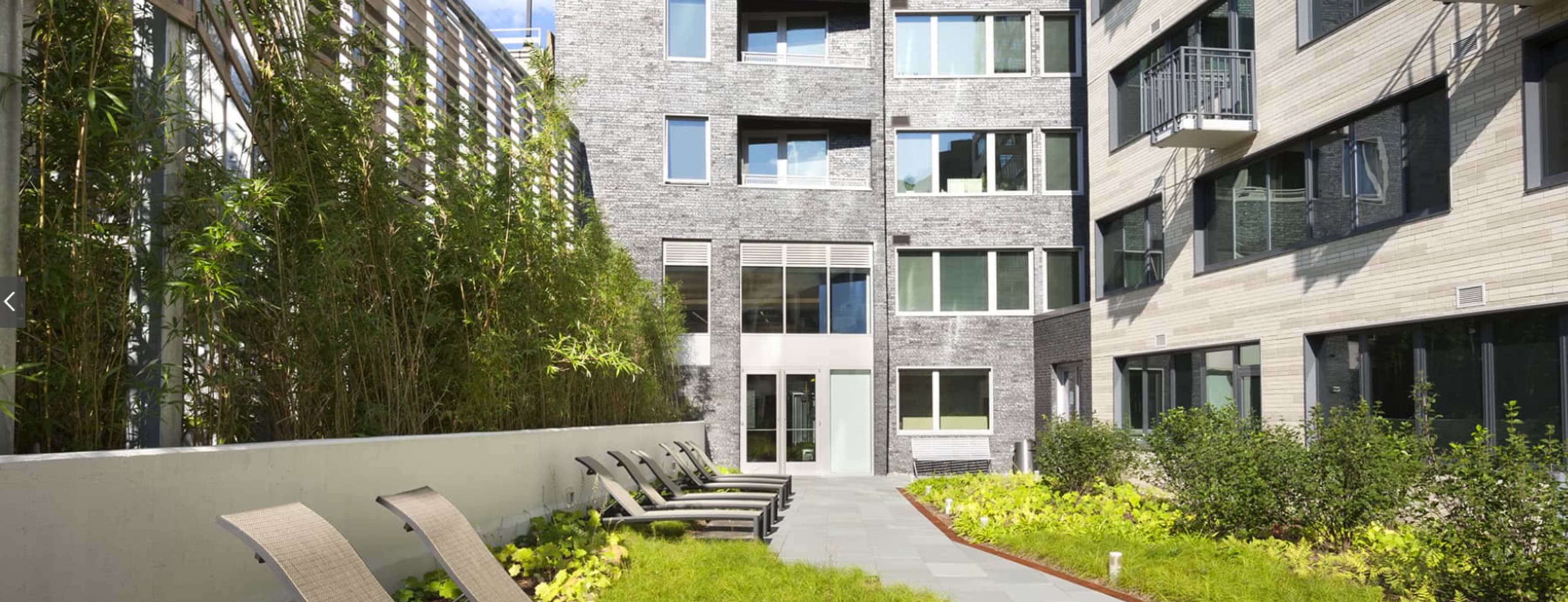 The image shows a modern courtyard with green plants, lounge chairs, and surrounding buildings.