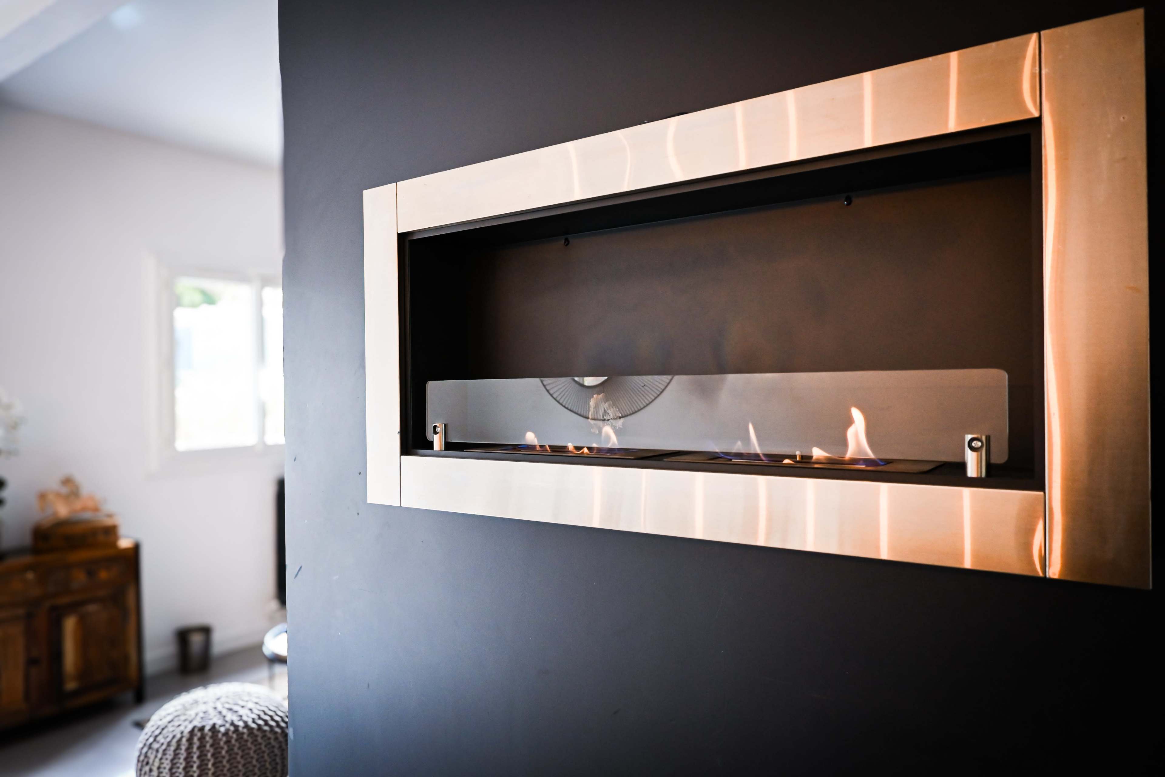 A modern wall-mounted fireplace with a sleek metallic frame displays a small flame against a dark wall.