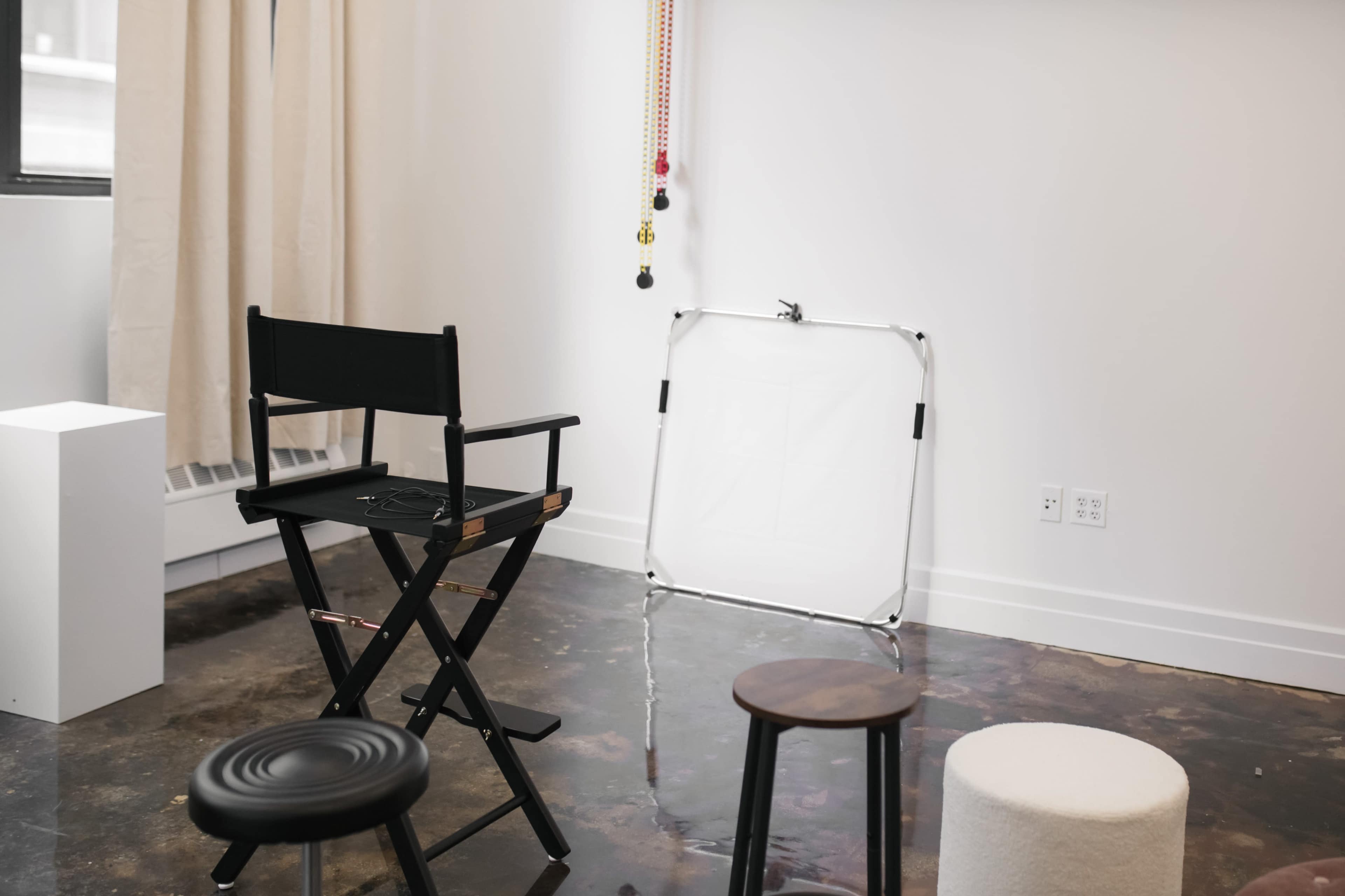 A black director's chair and two stools are arranged in a minimalist room with polished concrete flooring and a white wall.