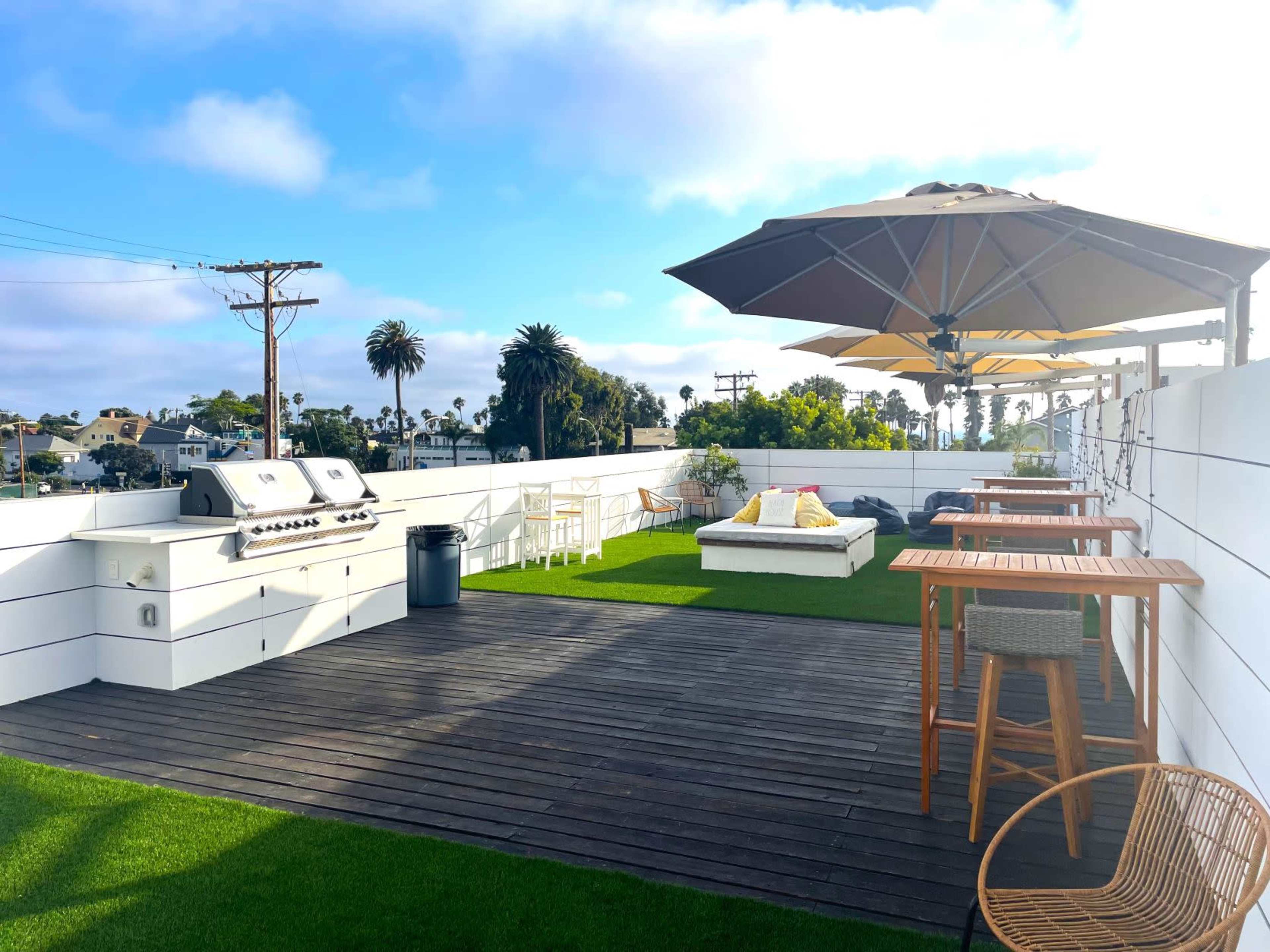 A rooftop terrace with a barbecue grill, seating areas under umbrellas, and artificial grass.