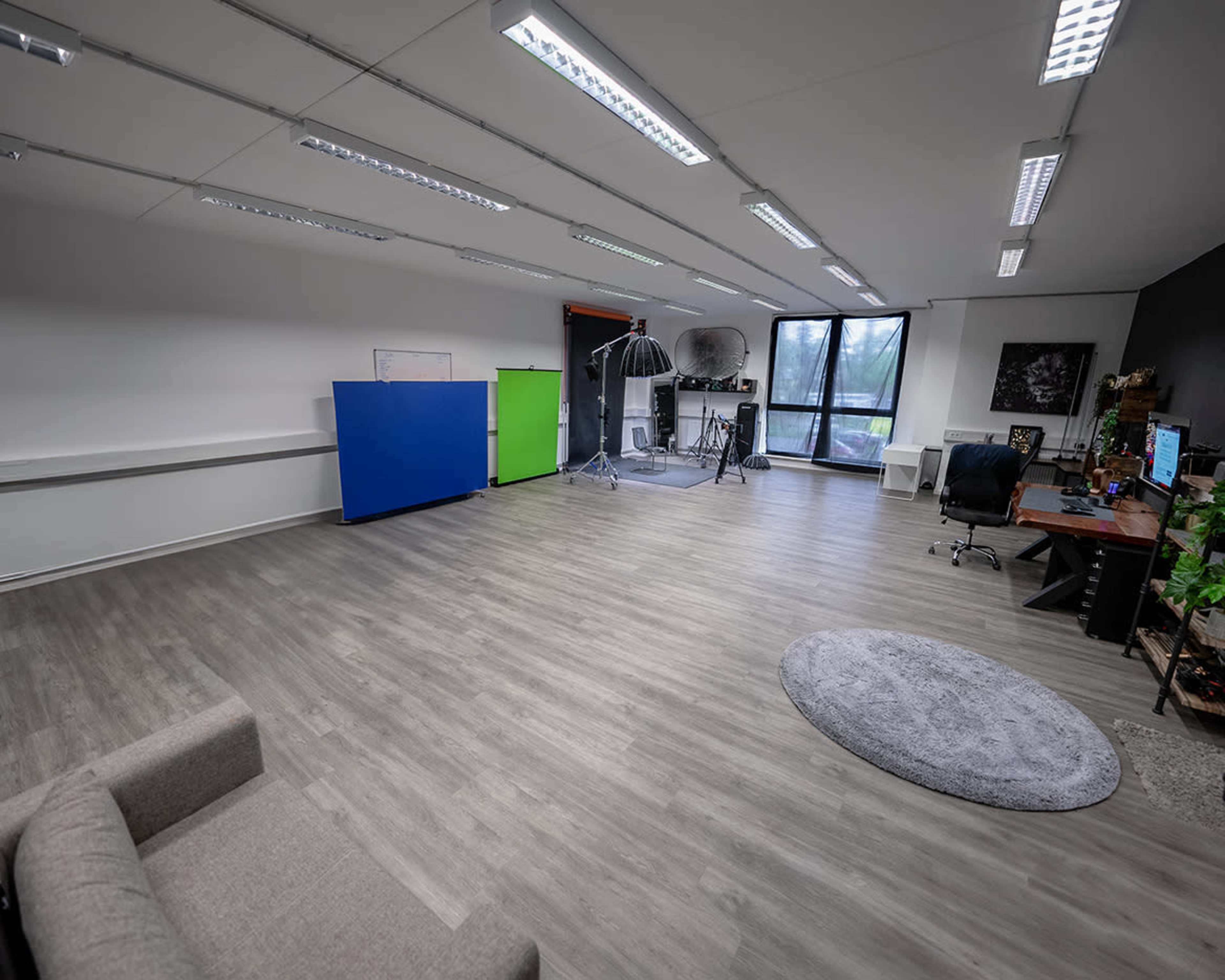 A spacious, modern studio with various colored backdrops, a large window, and minimal furniture.