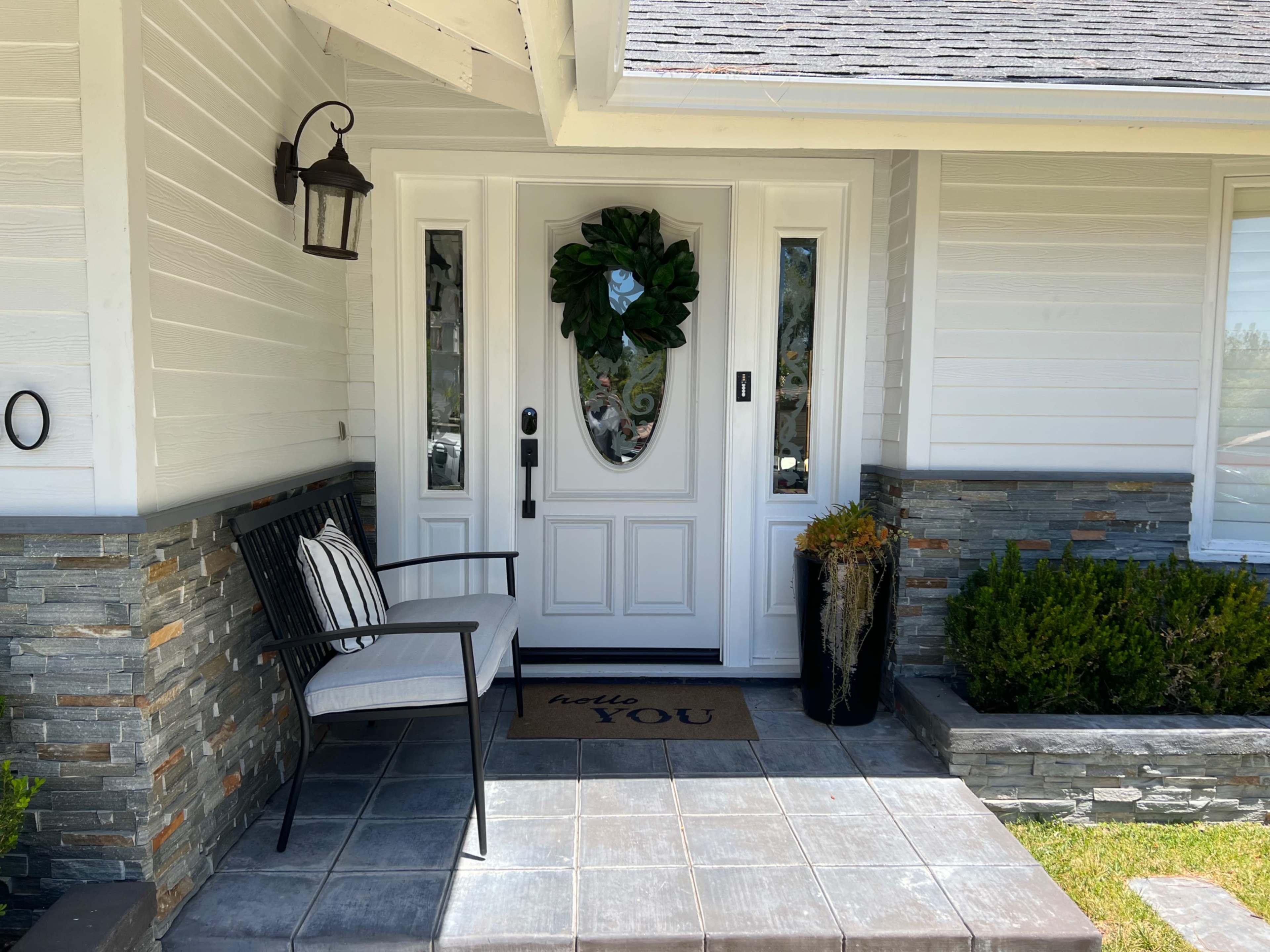 A front porch with a white door featuring decorative glass panels, flanked by a lantern and a welcome mat that reads "hello YOU."