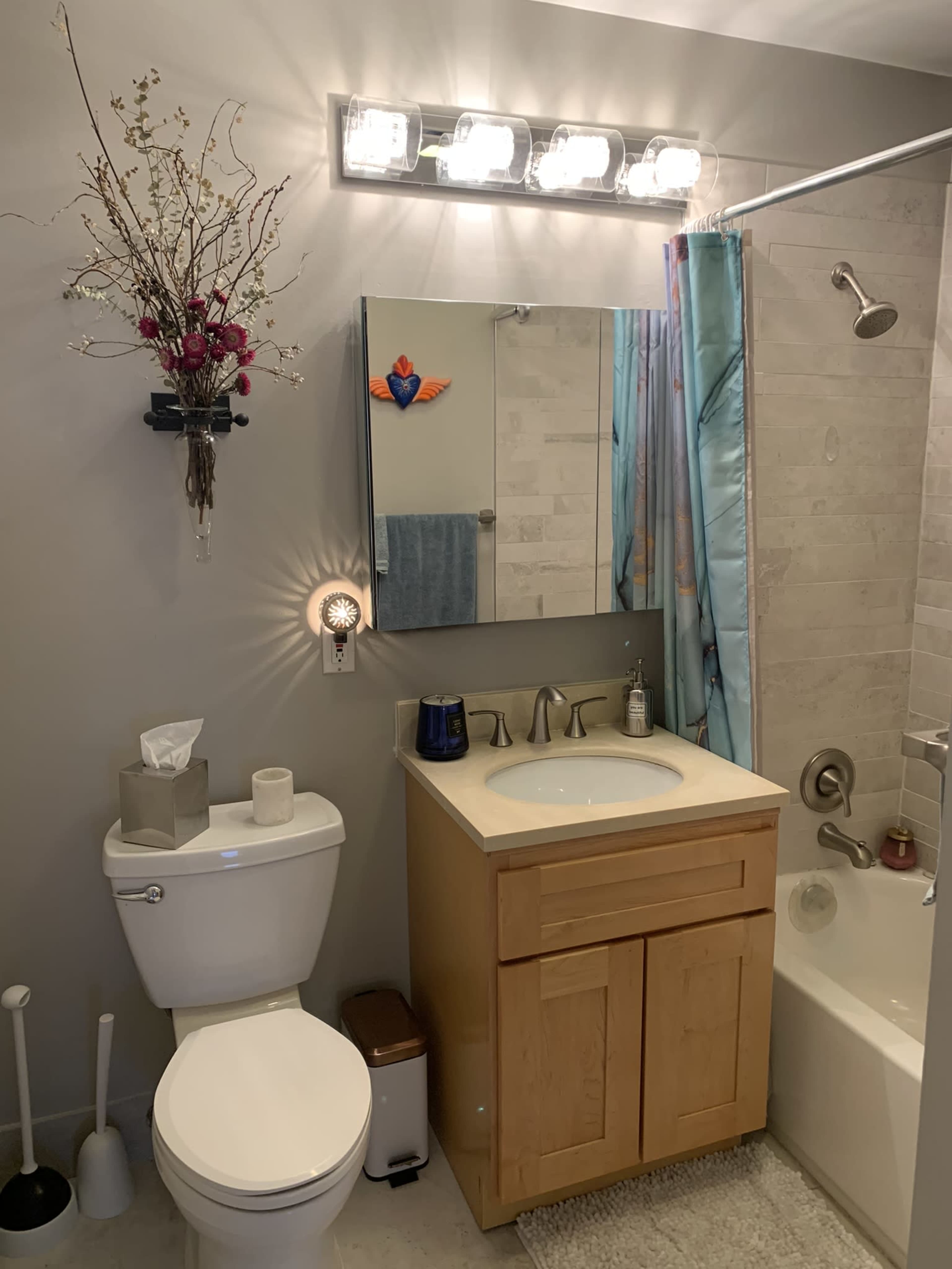 A modern bathroom featuring a toilet, a wooden vanity with a sink, and a shower-tub combination, all complemented by decorative elements and lighting.