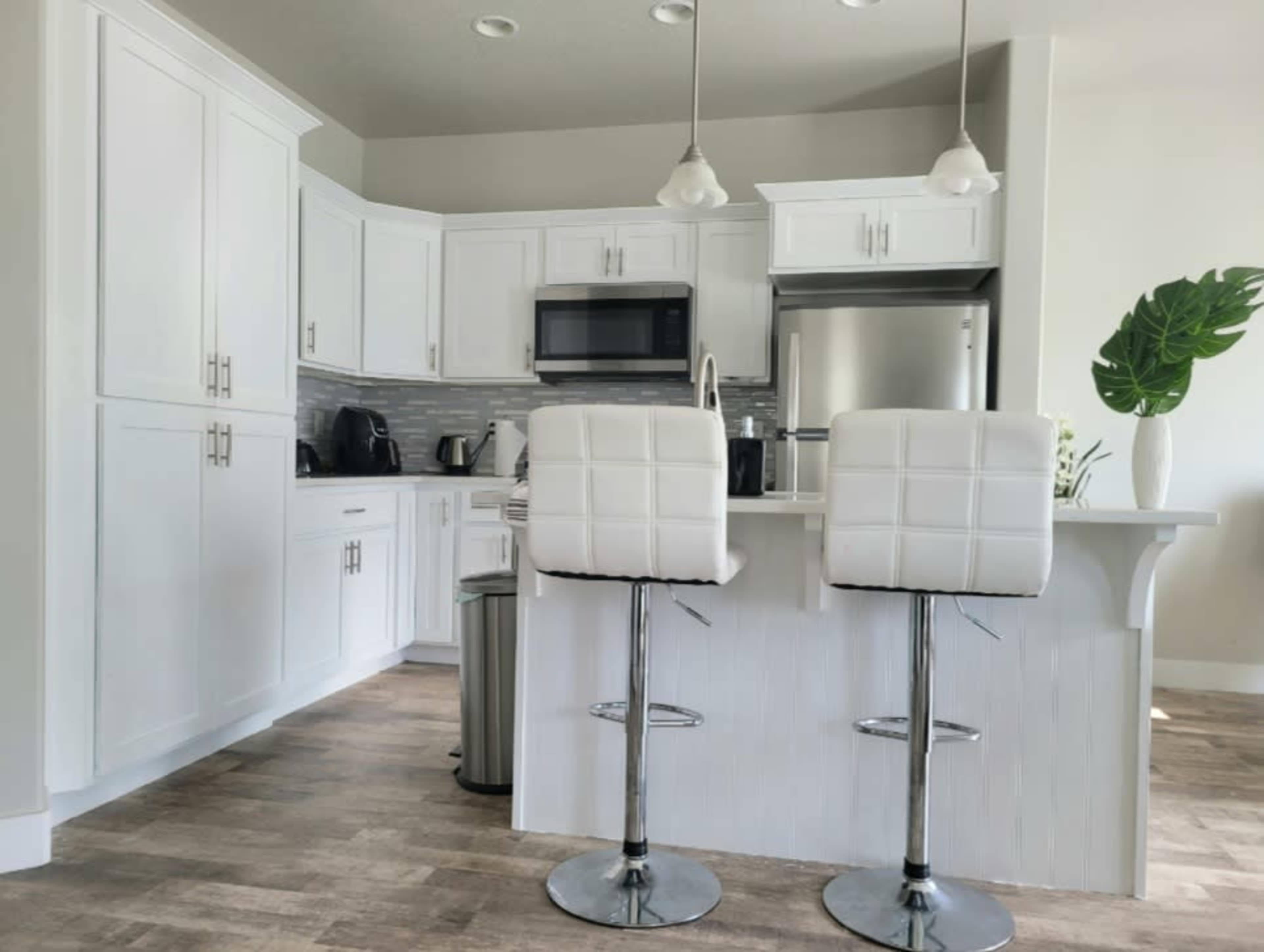 A modern kitchen features white cabinetry, stainless steel appliances, and two bar stools at a breakfast counter.