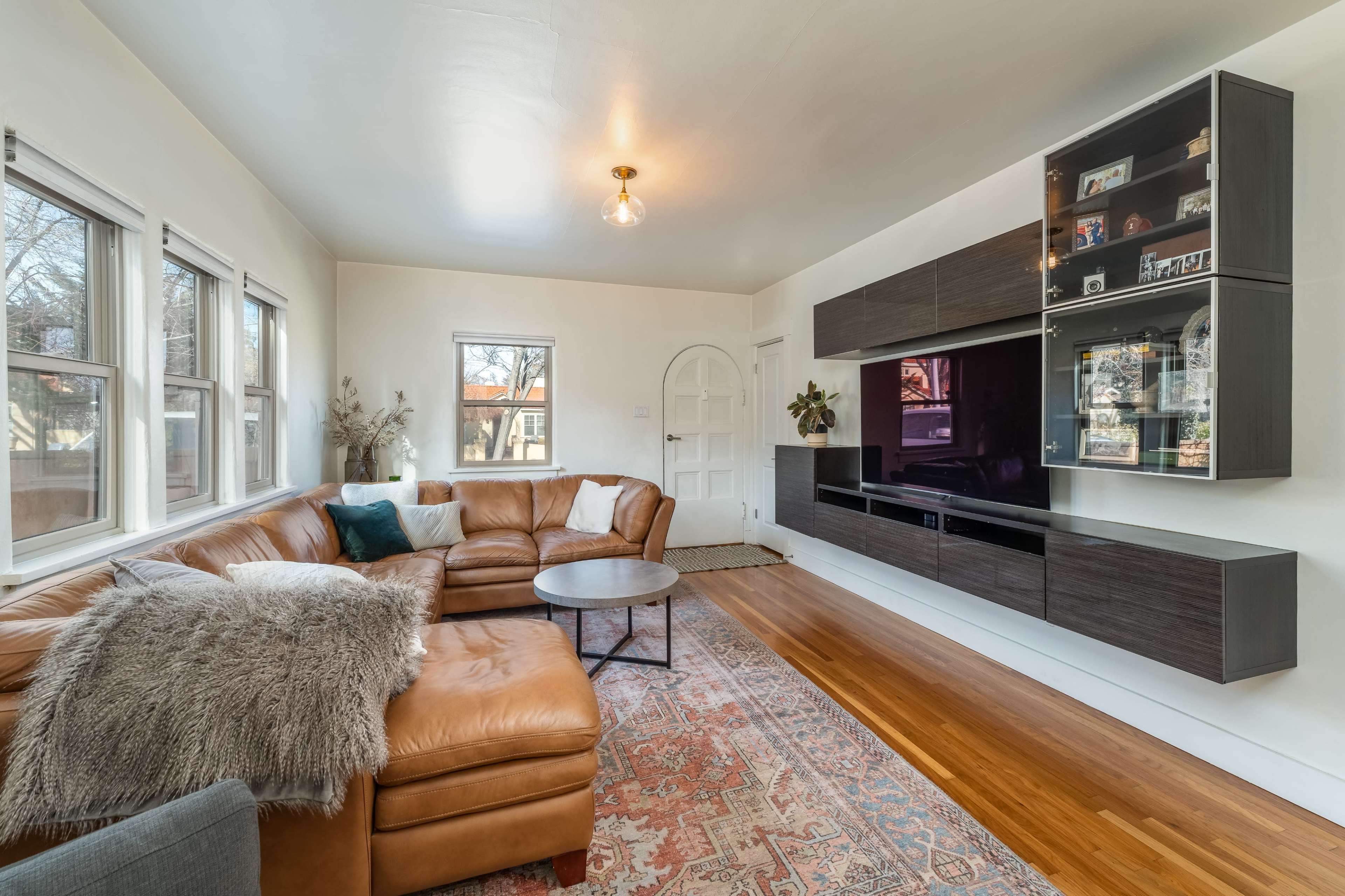 A modern living room with a brown leather sectional sofa, a round coffee table, and a wall unit housing a flat-screen TV and decorative items.