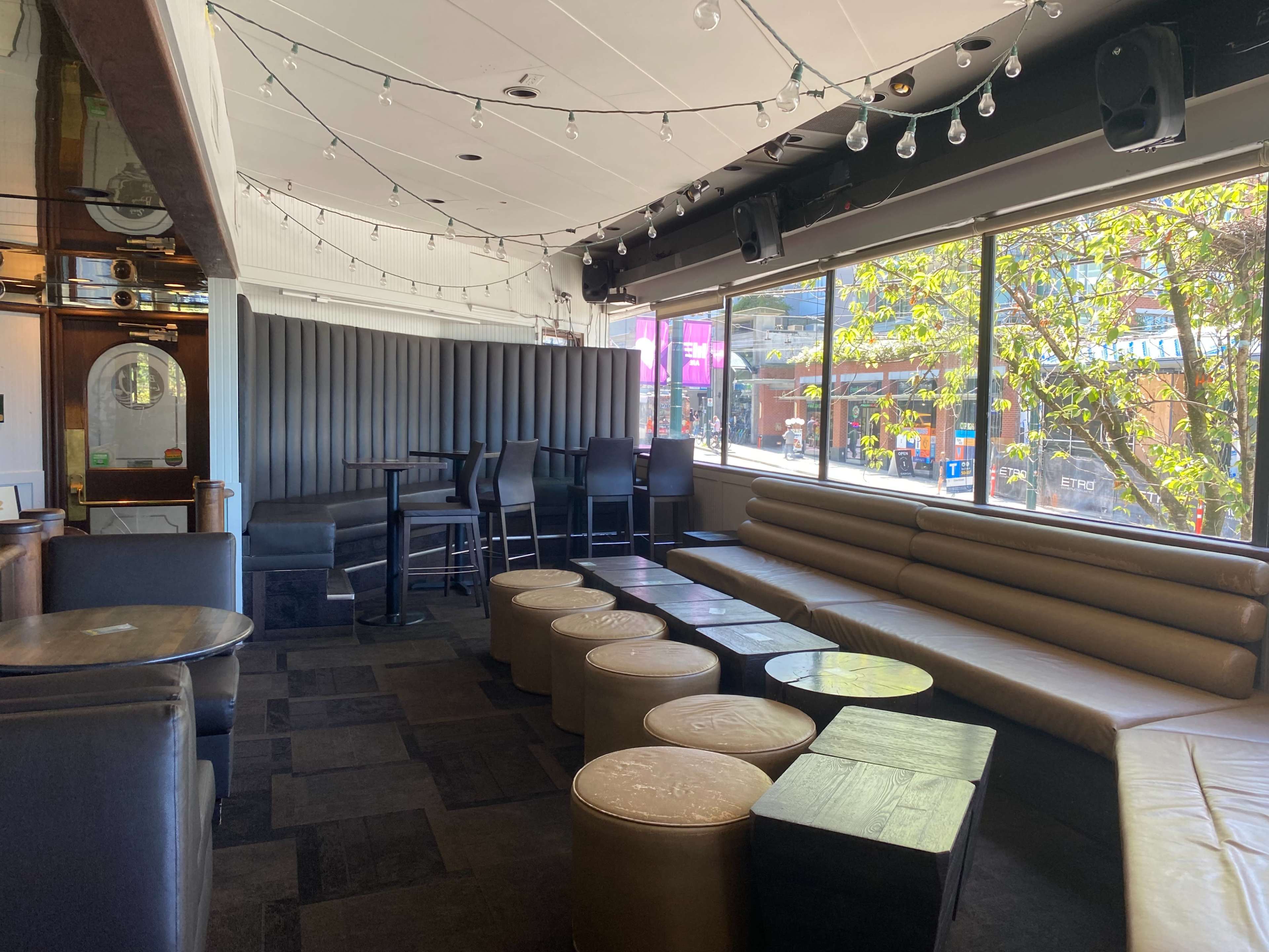 A spacious lounge area with seating along a large window, modern furniture, and light fixtures hanging from the ceiling.