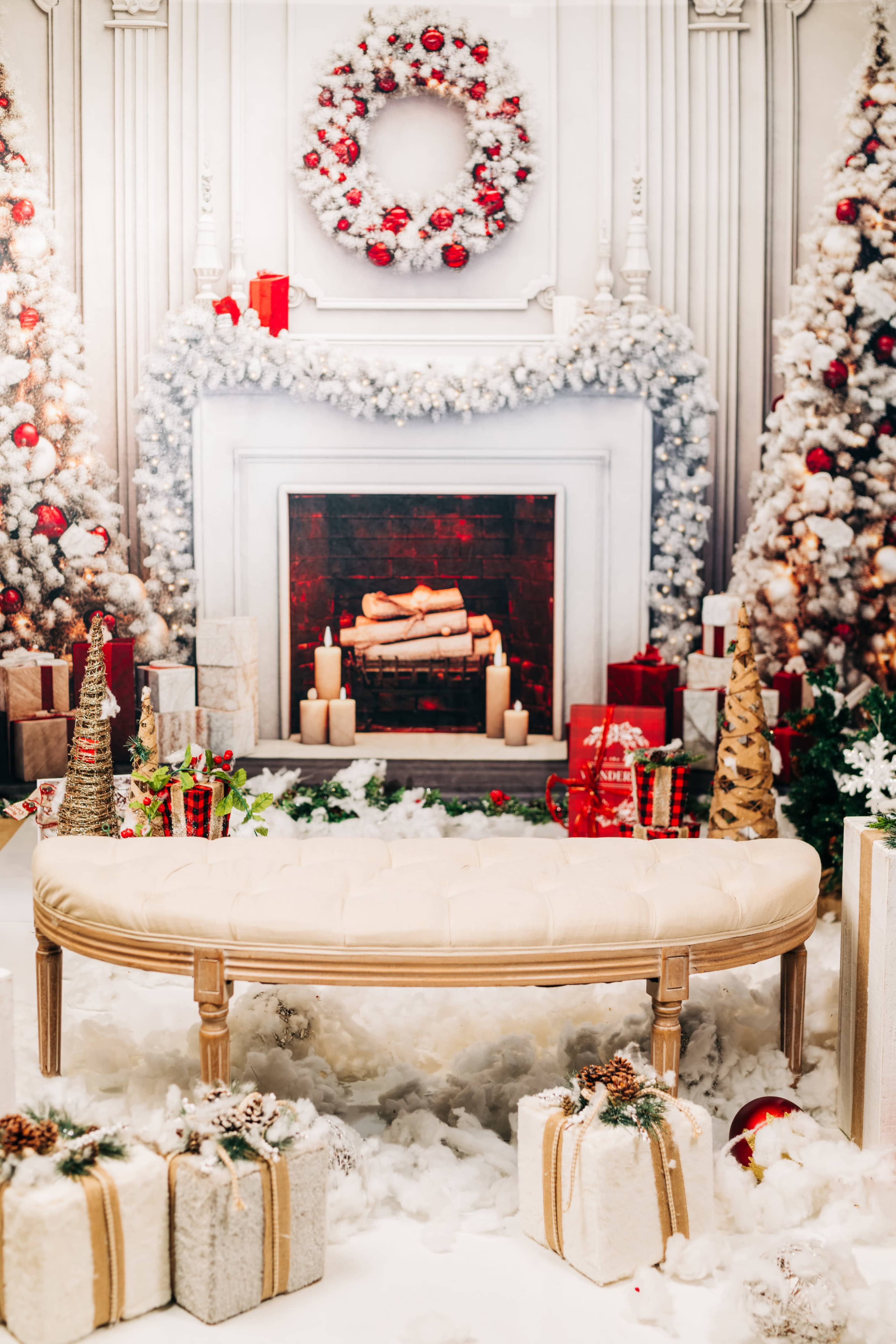 The scene features a decorated Christmas setting with a white mantelpiece, a fireplace, and a tufted bench surrounded by festive gifts and holiday decorations.
