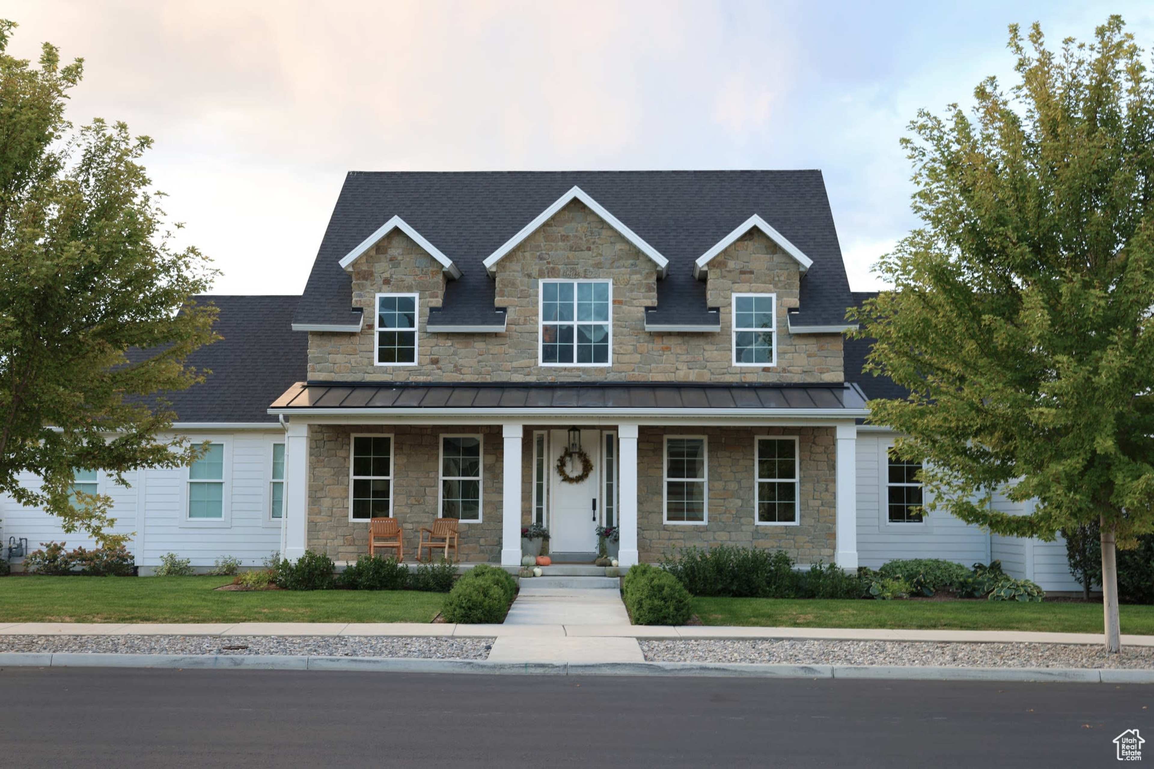 A large two-story house features a stone facade, a steep gable roof, and a front porch with wooden chairs.