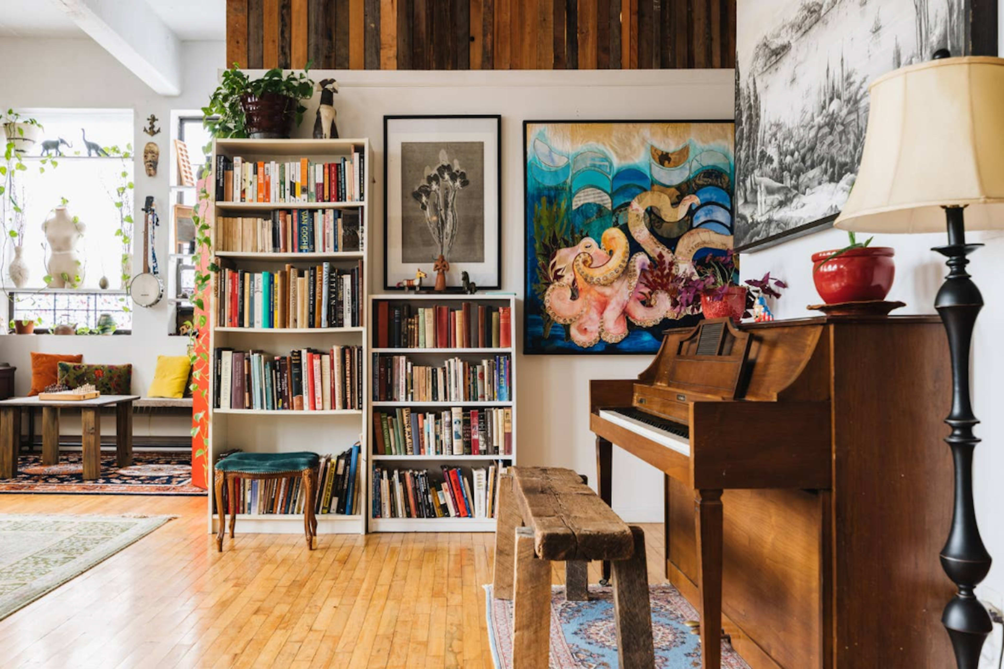 The image depicts a cozy interior space with a bookshelf filled with books, an upright piano, and colorful artwork on the walls, surrounded by various plants and decorative elements.