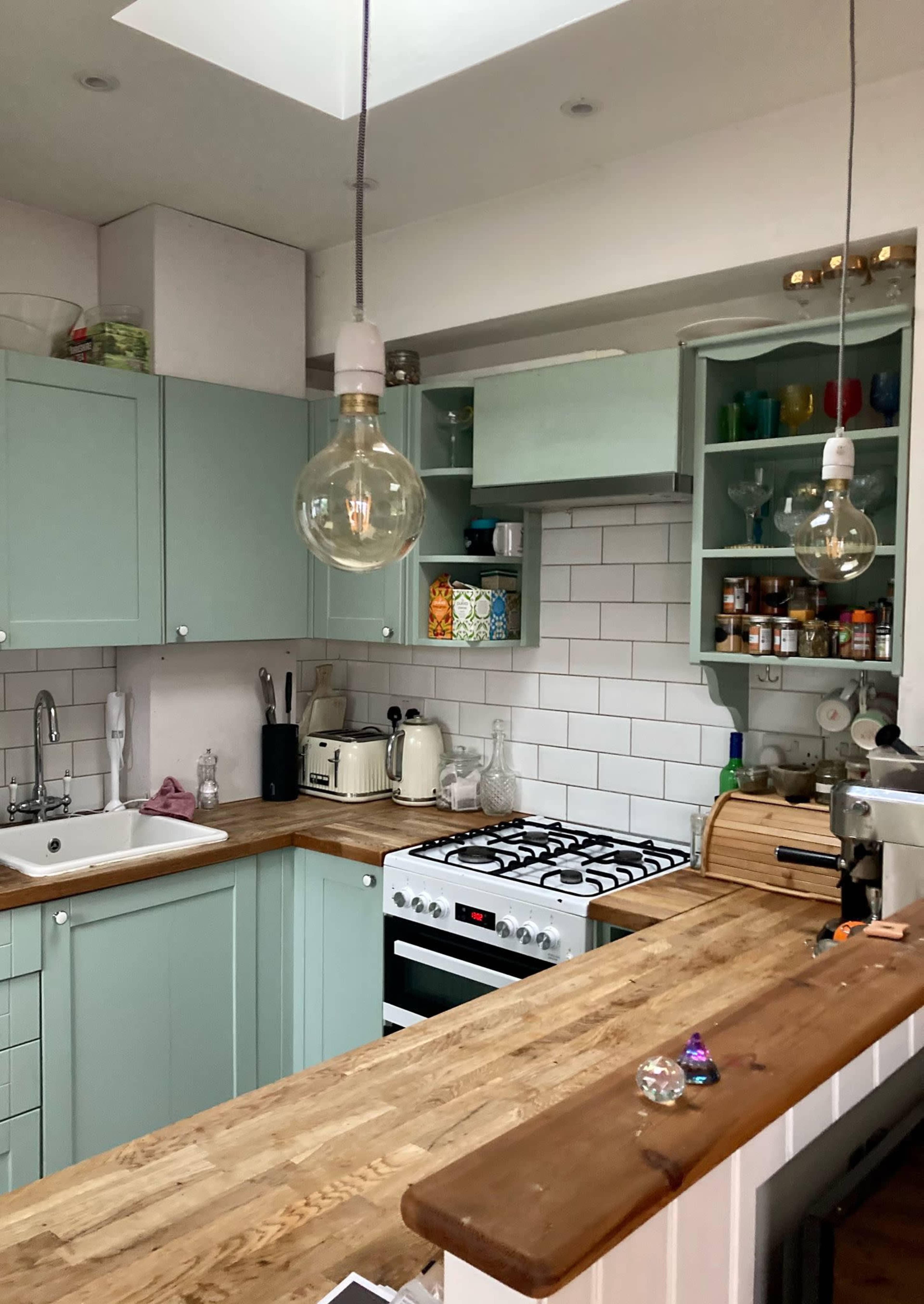 A modern kitchen features mint green cabinets, white subway tiles, a wooden countertop, and pendant lighting above the workspace.