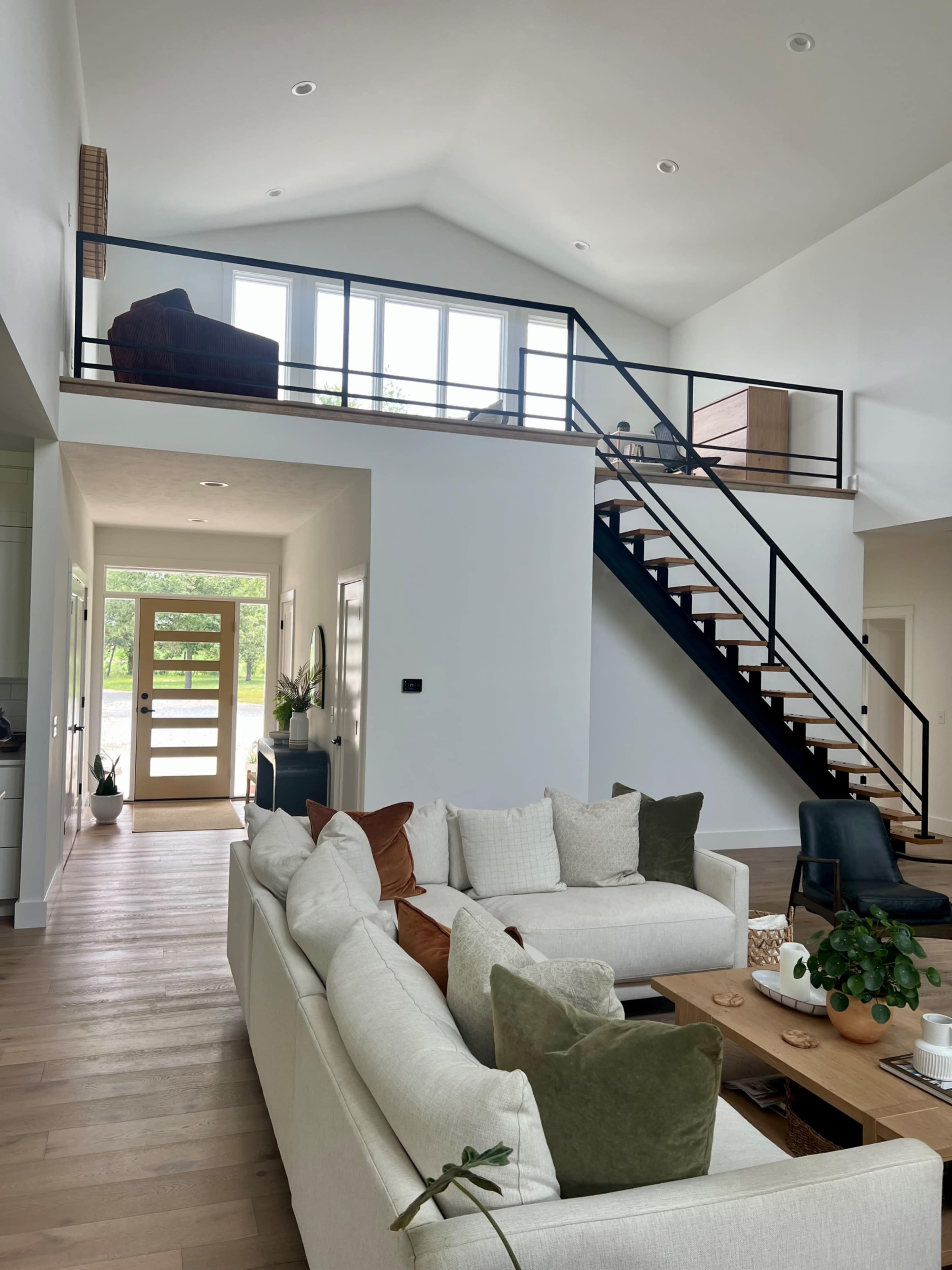 The image shows a modern open-concept living space with a large sofa, a wooden coffee table, and a staircase leading to an upper level.