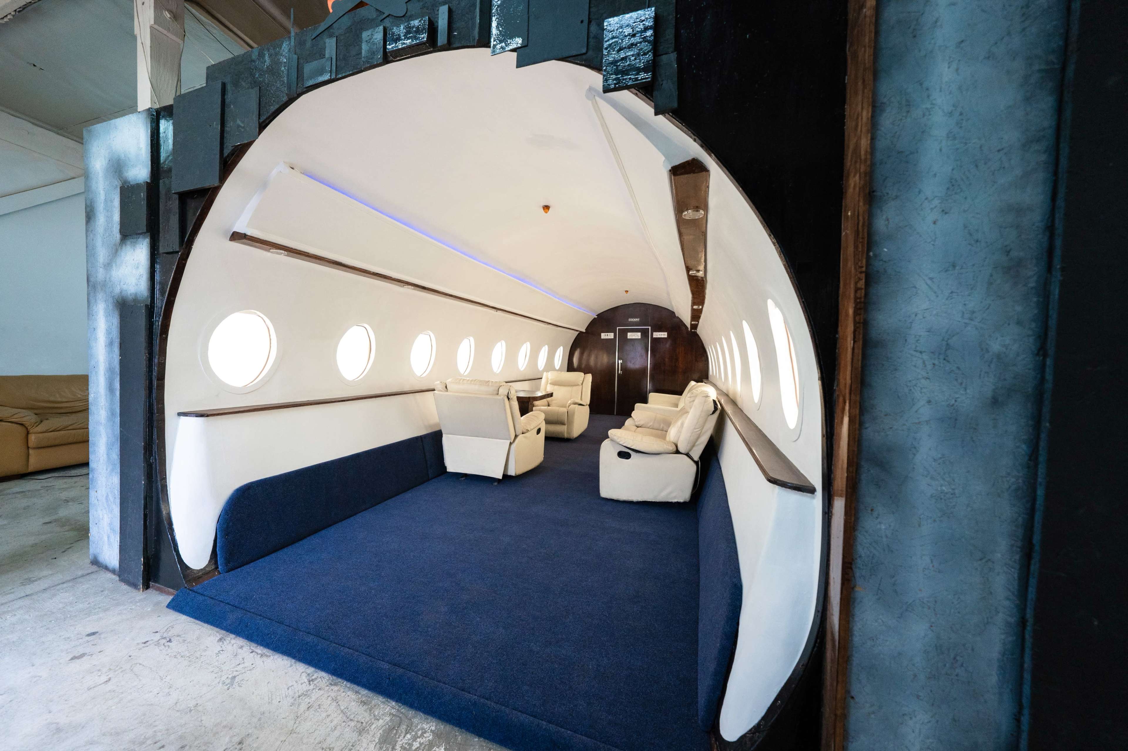 The interior of a space designed to resemble the fuselage of an airplane, featuring a curved entrance and white seating arranged along the sides.