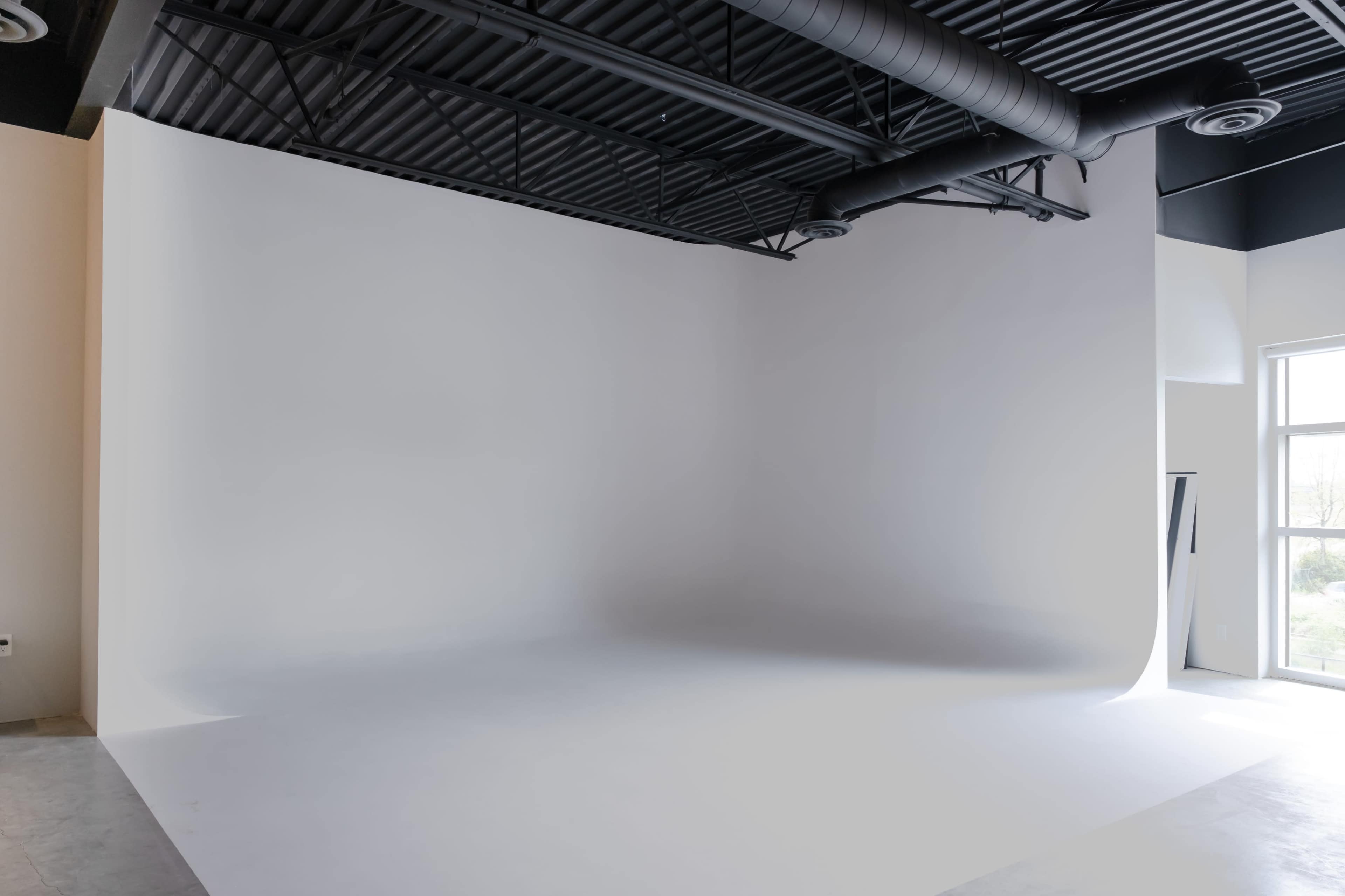 A spacious photography studio with a seamless white backdrop and large windows letting in natural light.