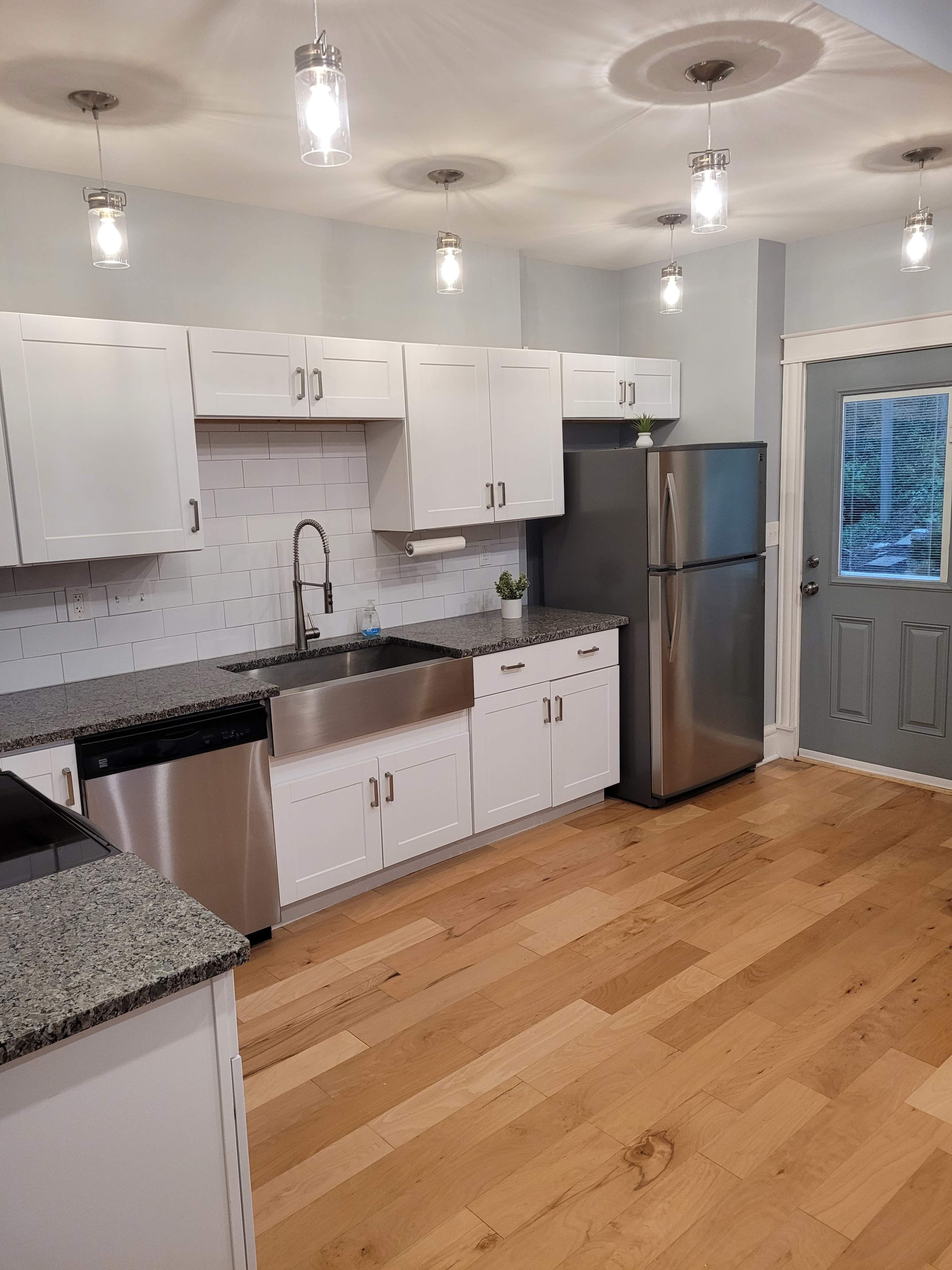 A modern kitchen features white cabinetry, stainless steel appliances, and a large sink with a polished granite countertop.