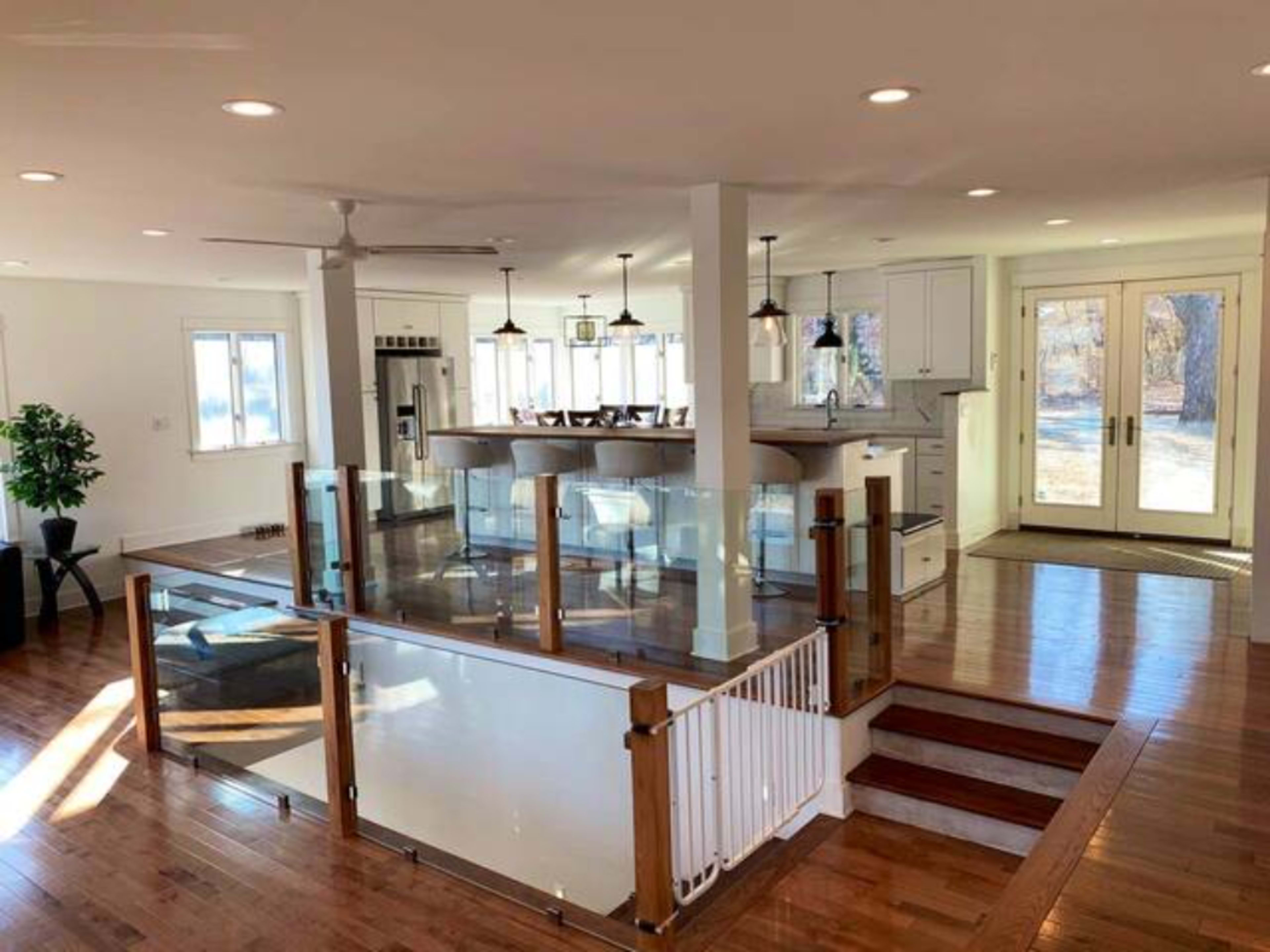 A spacious, modern interior with a kitchen area visible from an open living space, featuring hardwood floors and large windows.