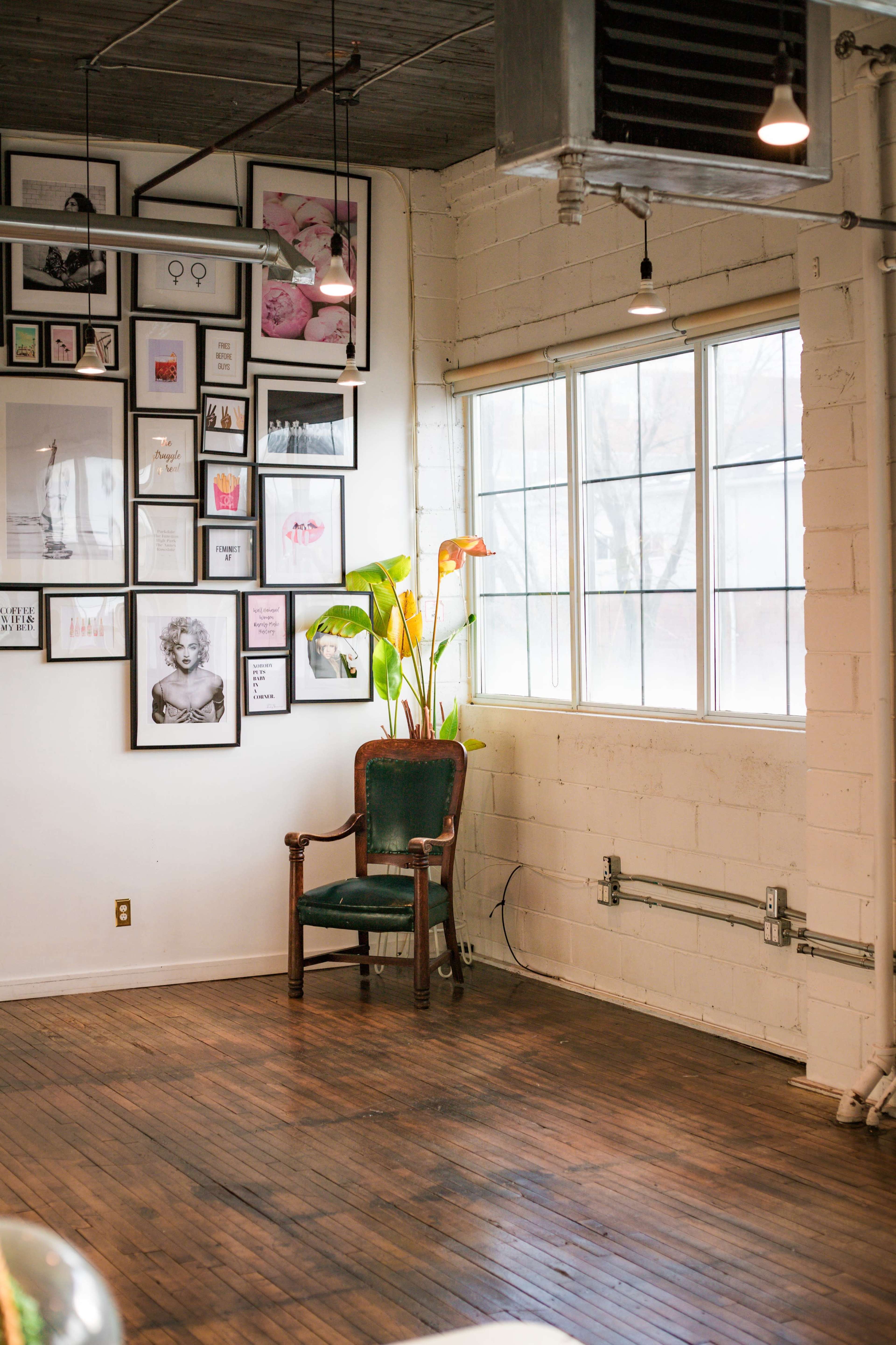 A vintage chair sits in a corner of a bright room adorned with a gallery wall of framed artwork and photographs.
