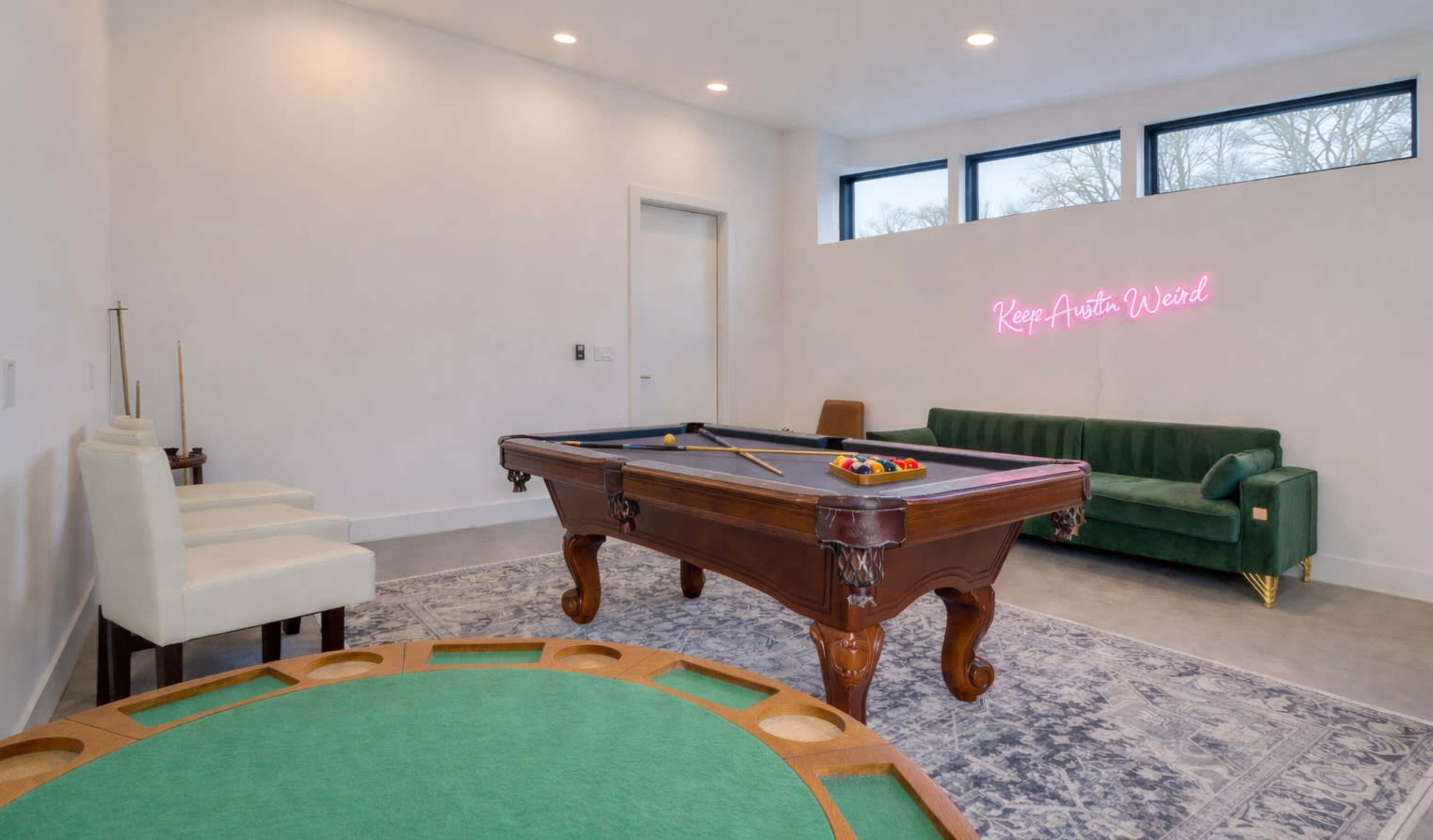 The image shows a modern game room with a pool table, a green couch, and a circular game table.
