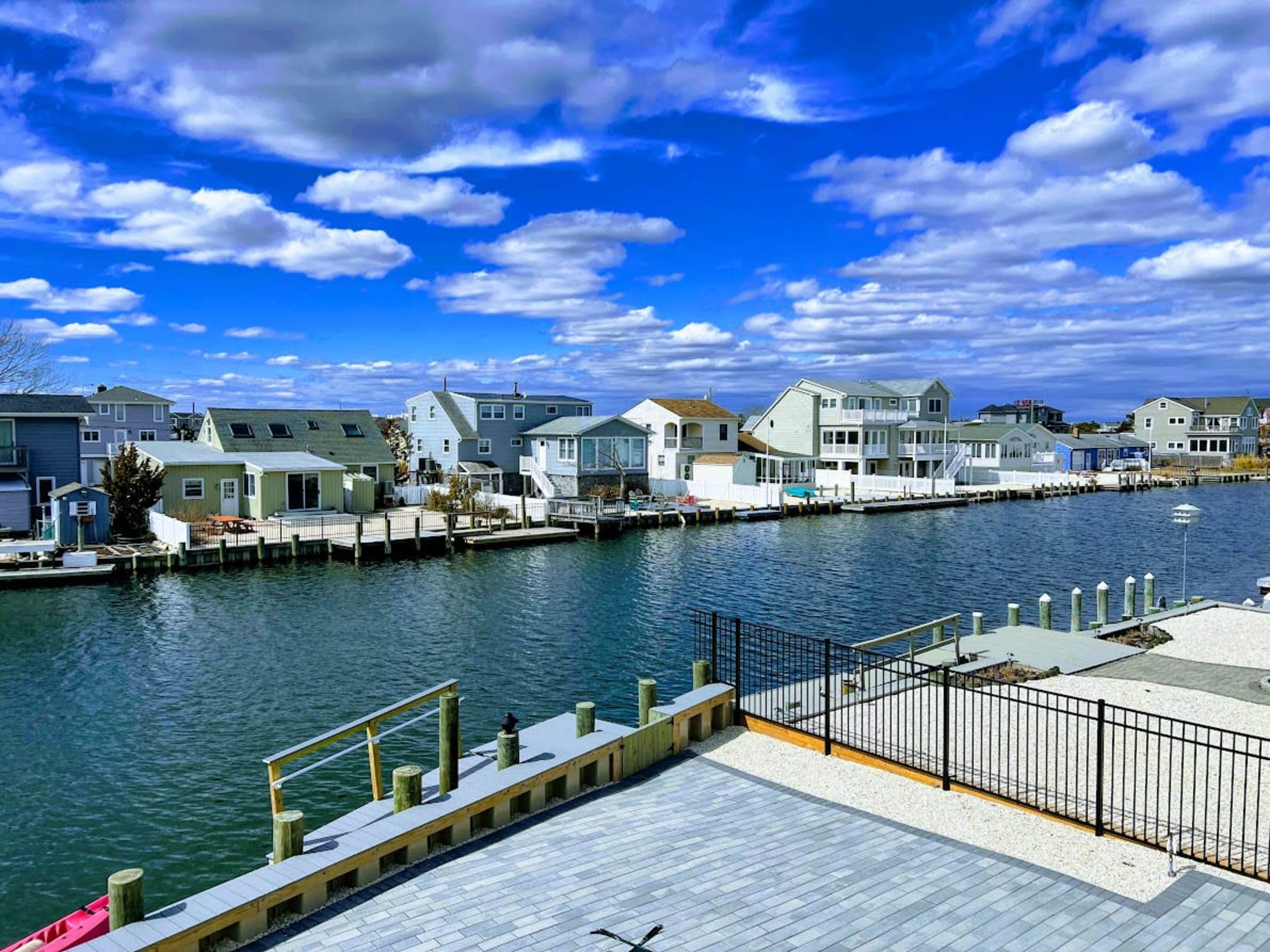 The image shows a calm waterway lined with houses and docks under a cloudy blue sky.
