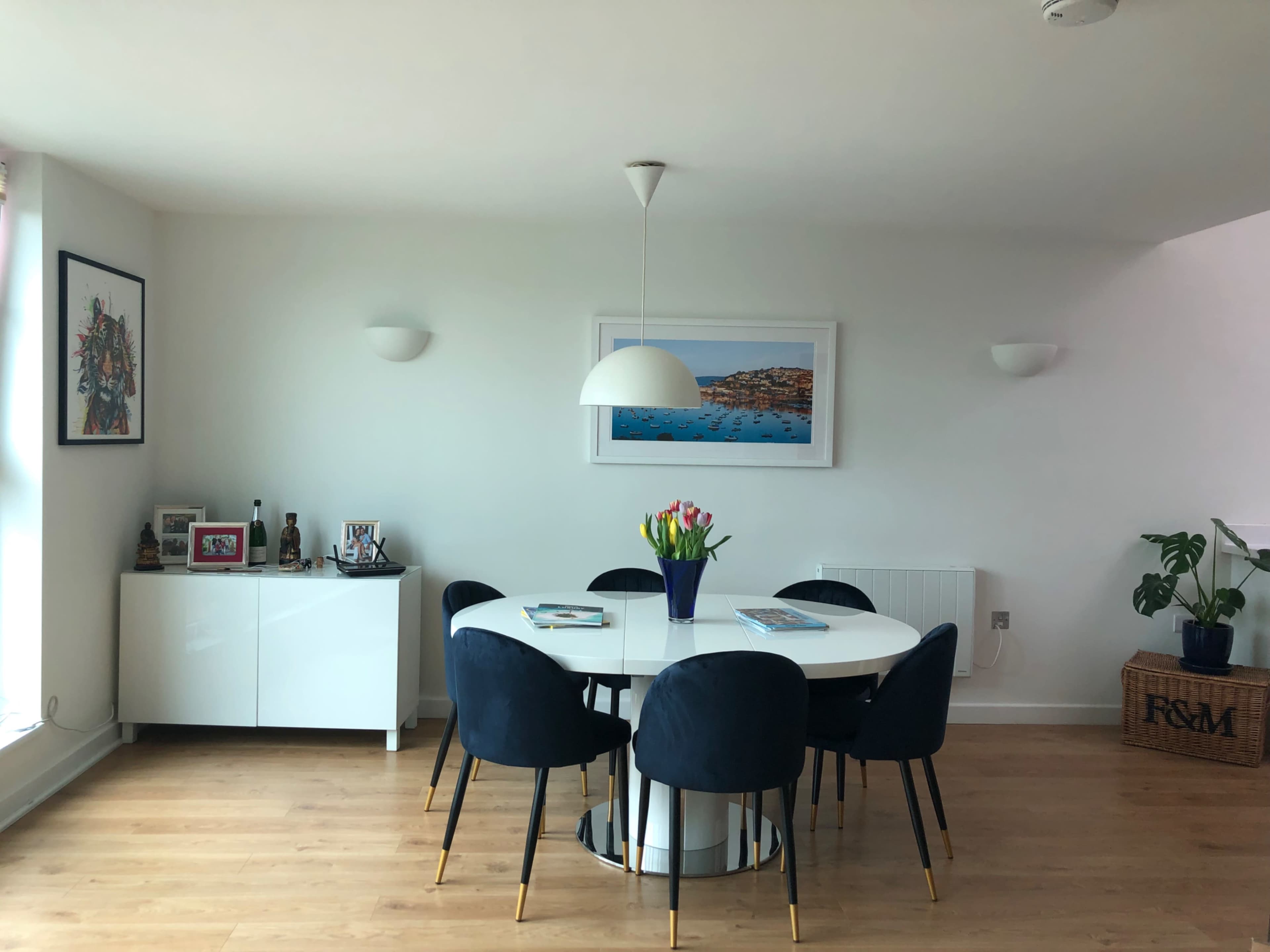 A dining area features a round white table surrounded by six black chairs, with a vase of colorful tulips and framed artwork on the walls.